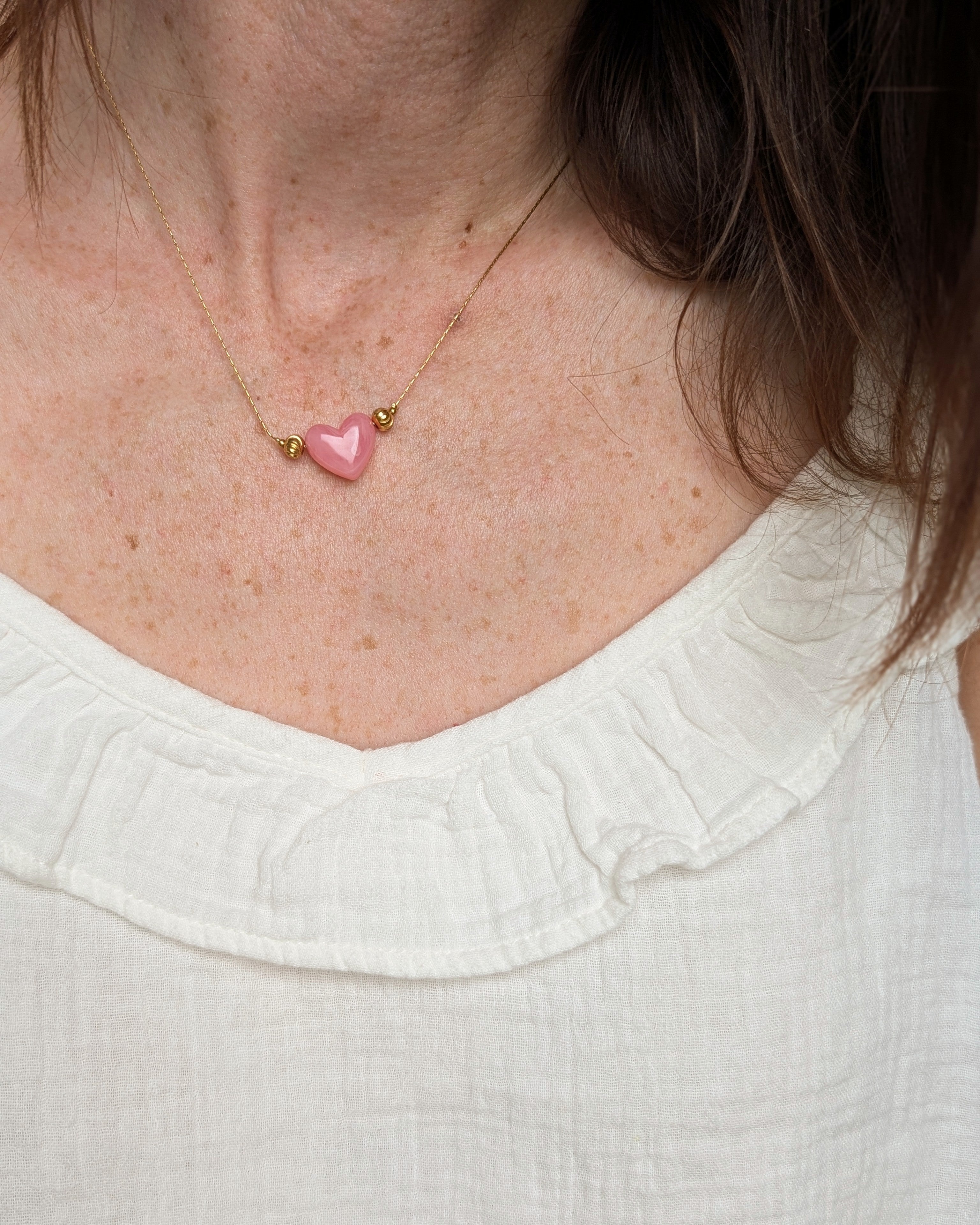 Collier Aimée perle coeur en résine rose tendre et acier inoxydable doré porté par une femme. Création fait main La Tête dans les Nétoiles