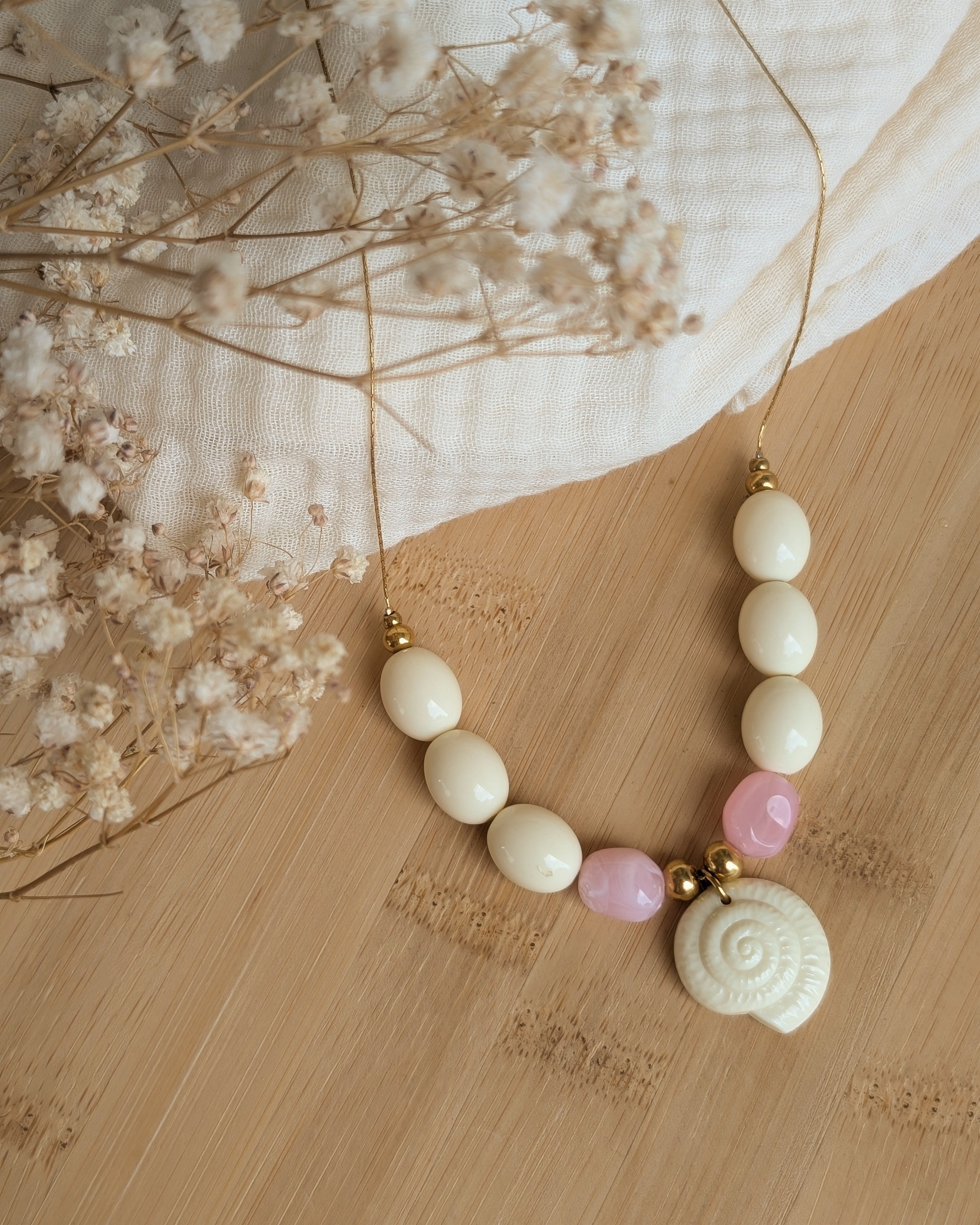 Collier Azura coquillage et perles en résine posé sur plateau en bois et gaze de coton. Création artisanale La Tête dans les Nétoiles 