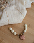 Collier Azura en entier sur plateau en bois. Perles crème et marron forme olive et pendentif coquillage ammonite marron clair. Perles en résine et maille en acier inoxydable. Création artisanale La Tête dans les Nétoiles 