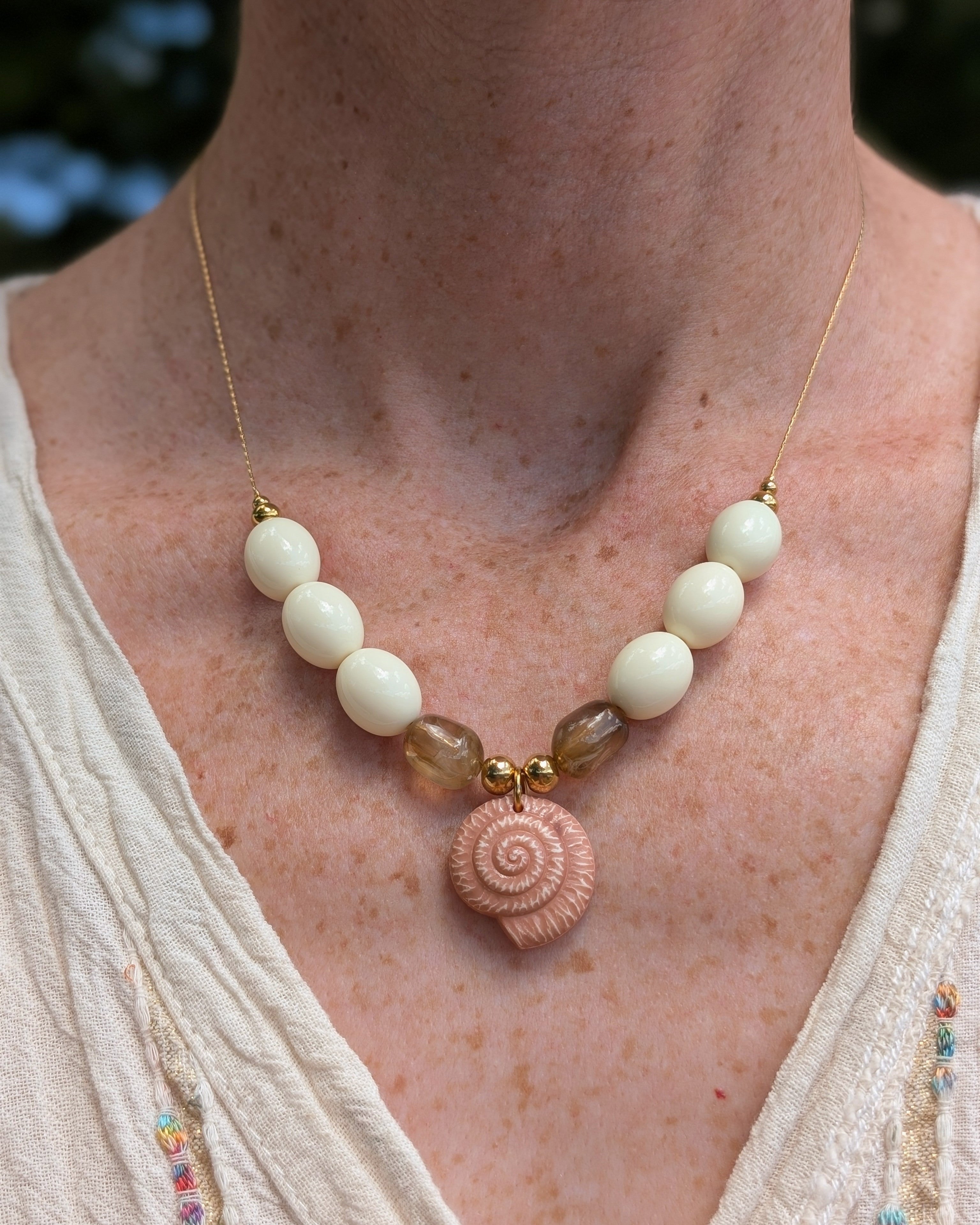 Collier Azura pees en résine clair et marron clair. Porté par une femme avec une robe en lin. Création artisanale La Tête dans les Nétoiles 