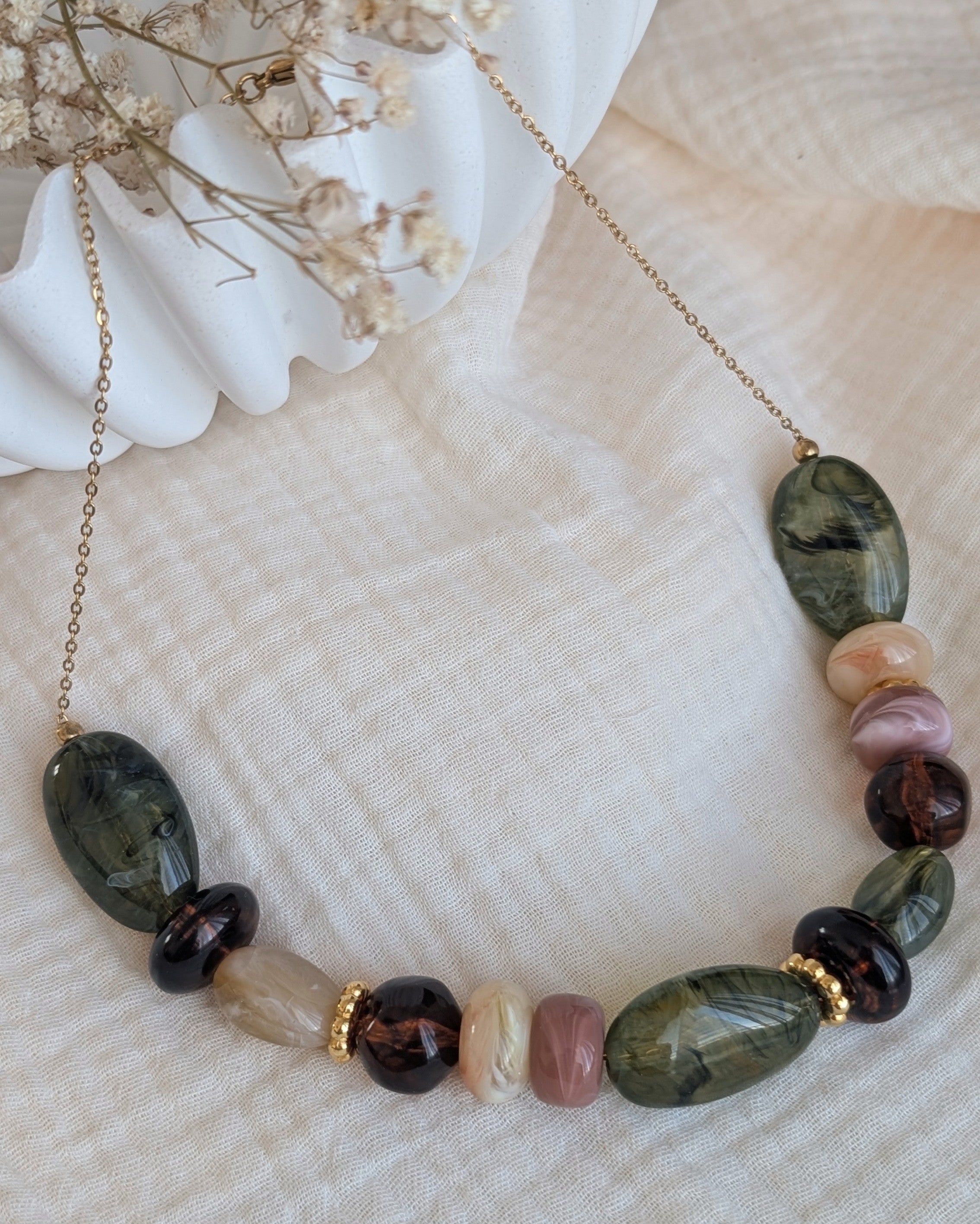 collier GABIE nuances de vert et d'ambre sur fond de gaze de coton. Perles en résine irréfulières enfilées sur chaîne maille forçat. Création artisanale La Tête dans les Nétoiles
