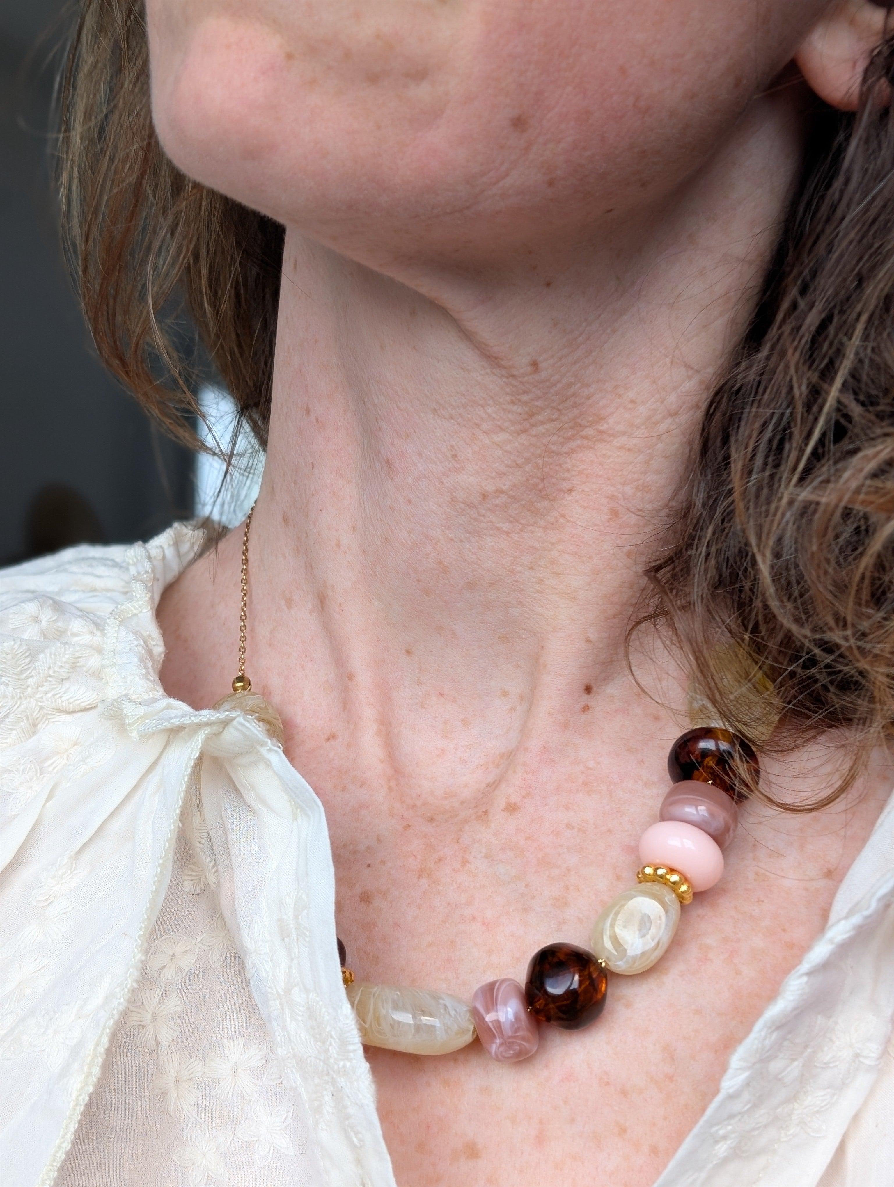 collier GABIE perles résines claires ambrées rose poudre perles irrégulières porté par une femme. Création artisanale La Tête dans les Nétoiles