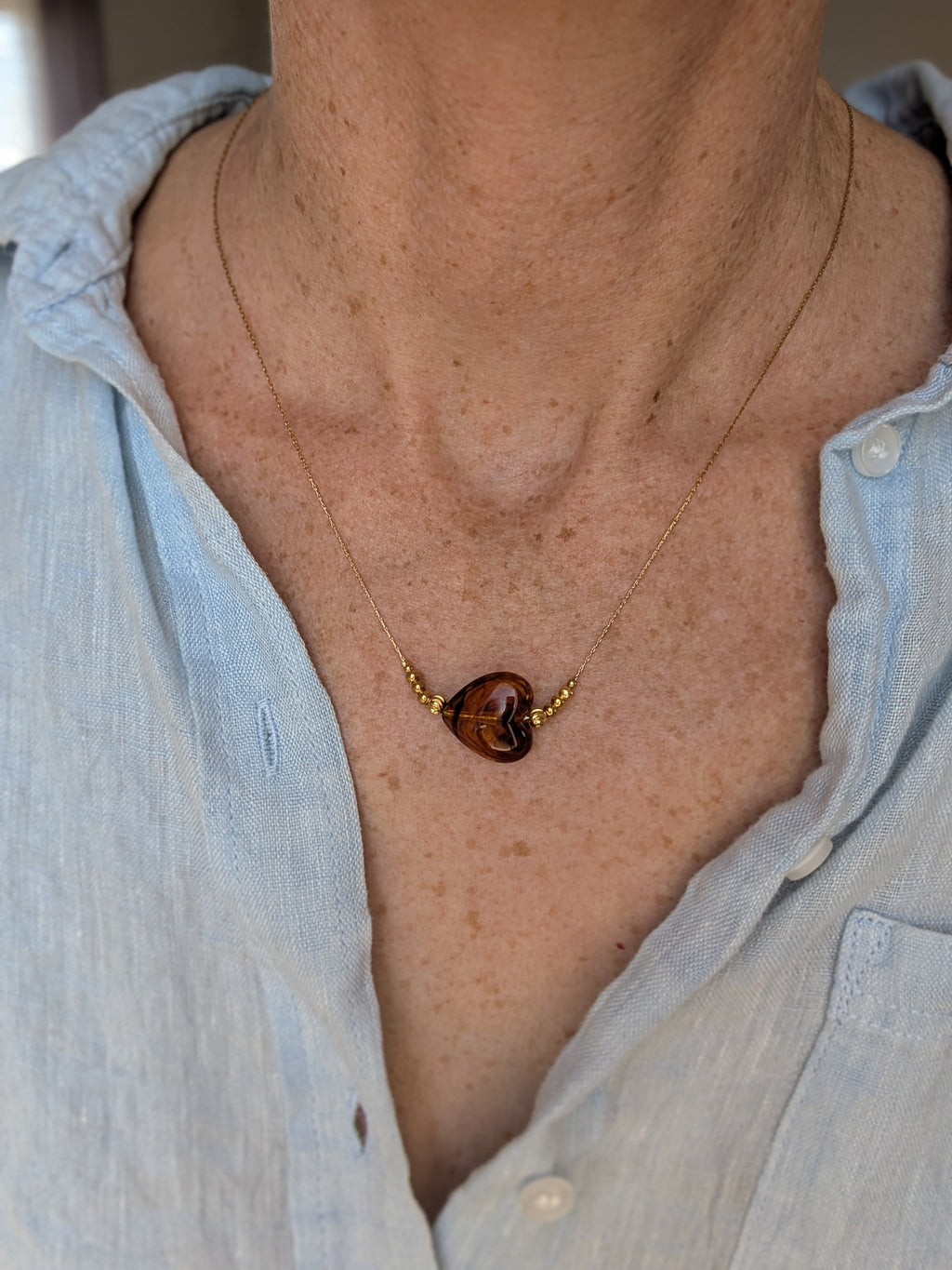 Collier Marcelle porté au plus long. Coeur en résine ambre caramel. Sur maille fine serpentine en acier inoxydable. Création artisanale La Tête dans les Nétoiles.