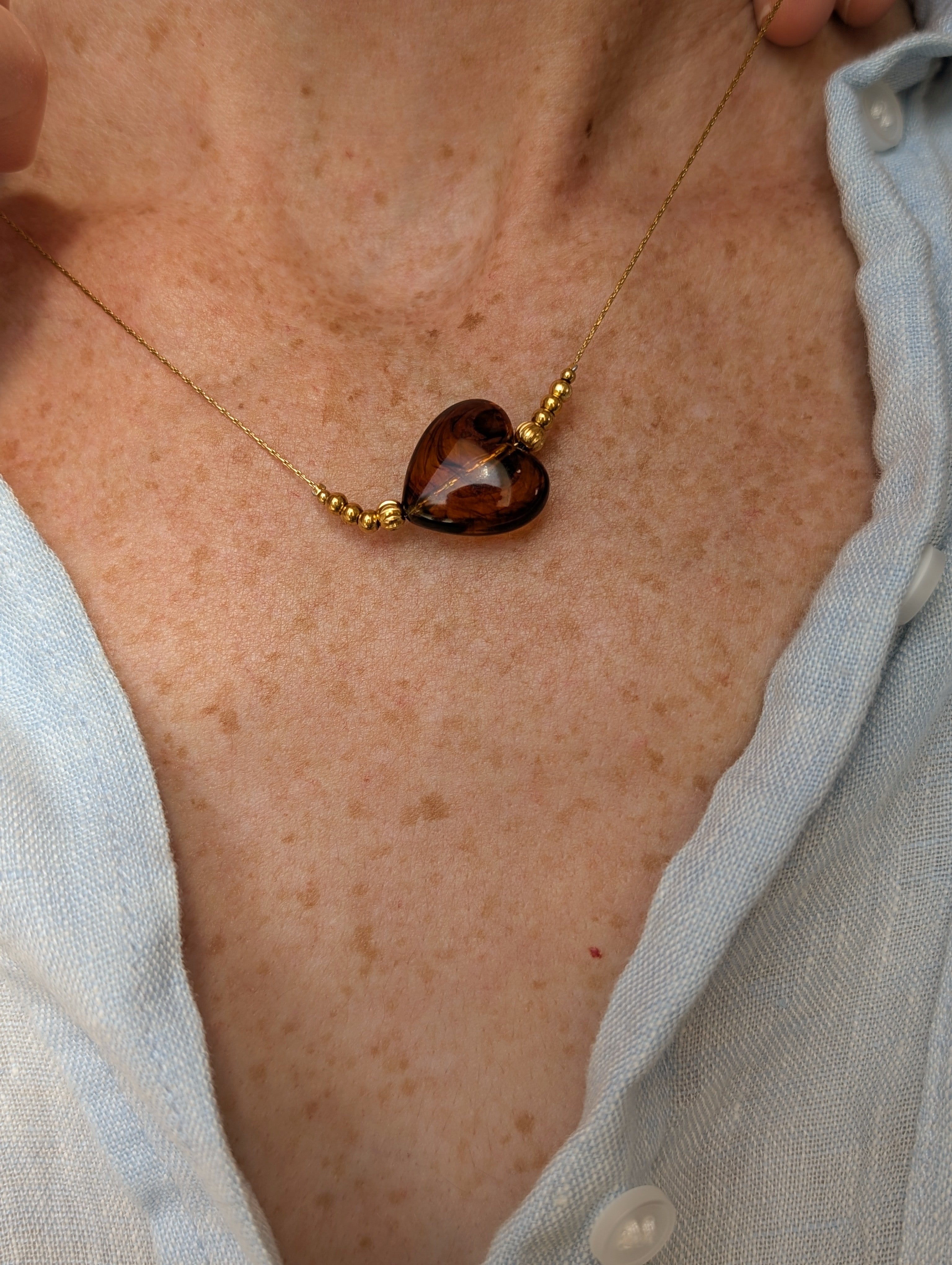 Collier Marcelle porté au plus court. Coeur en résine ambre caramel. Sur maille fine serpentine en acier inoxydable. Création artisanale La Tête dans les Nétoiles.