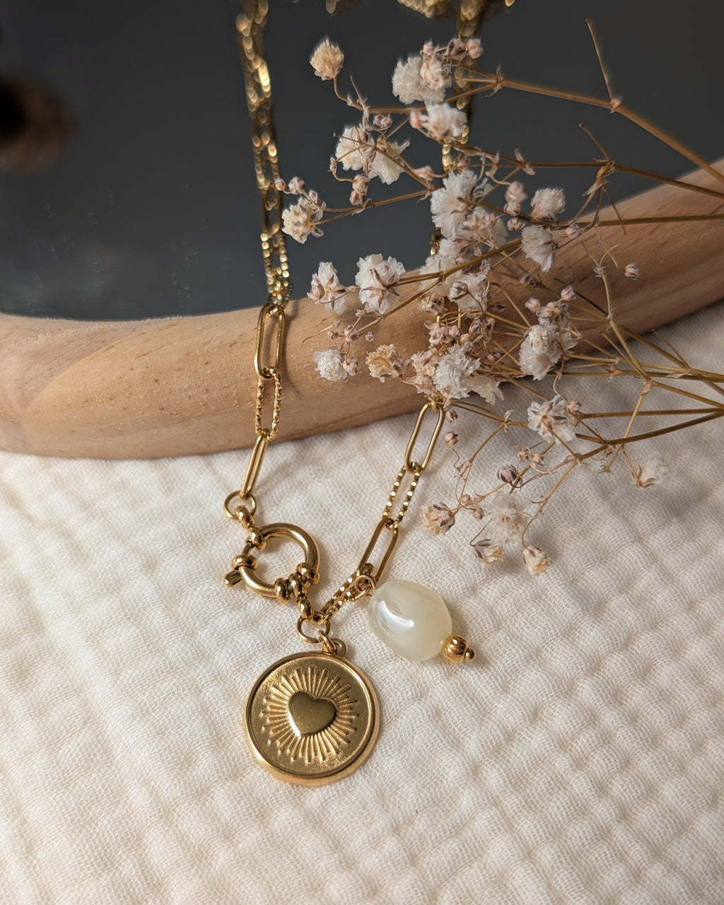 Collier Nahee pendentif coeur radiant et perle beige en resine sur chaine trombone. Posée sur gaze de coton et miroir. Créations artisanales La Tête dans les nétoiles.