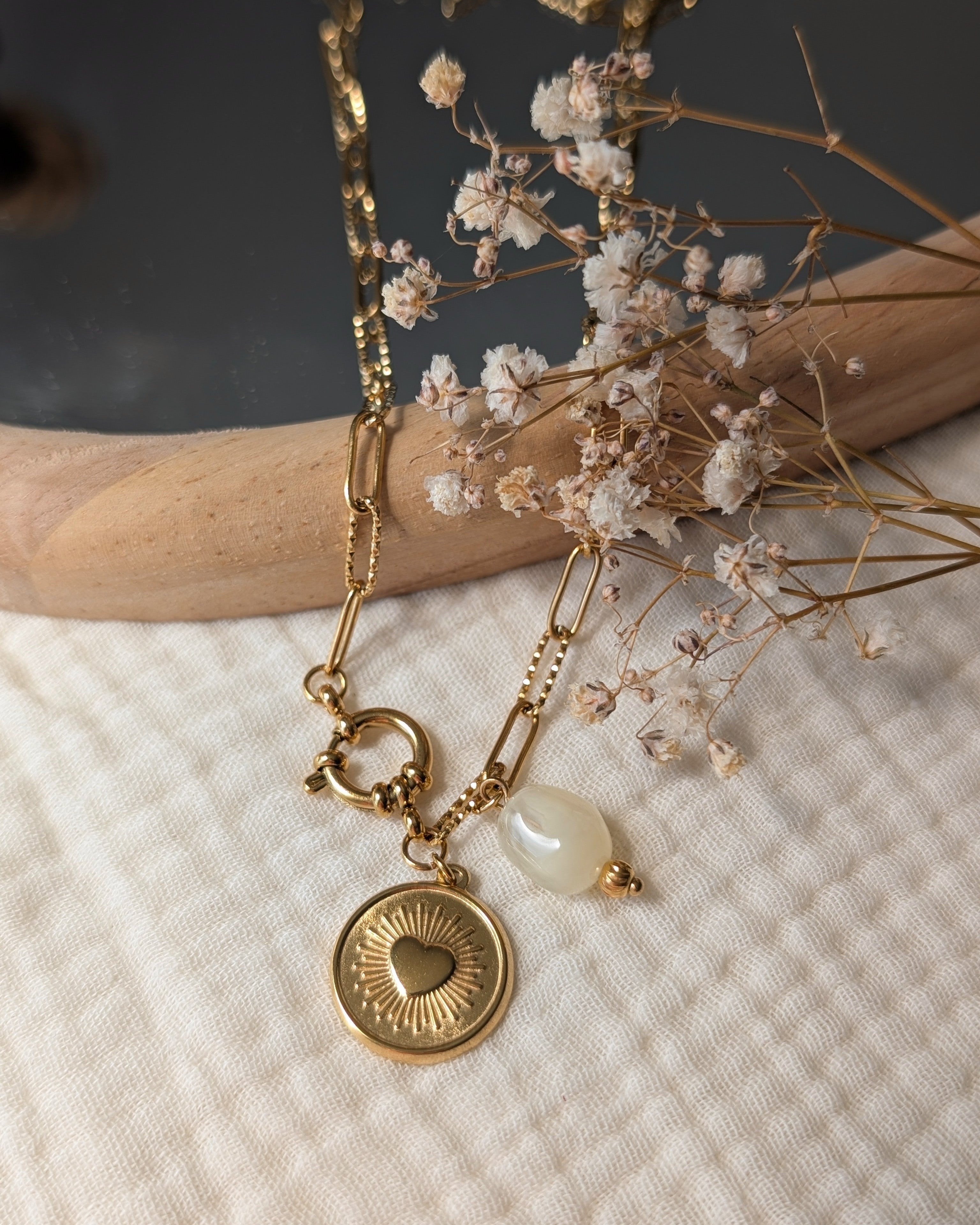 Collier Nahee pendentif coeur radiant et perle beige en resine sur chaine trombone. Posée sur gaze de coton et miroir. Créations artisanales La Tête dans les nétoiles.