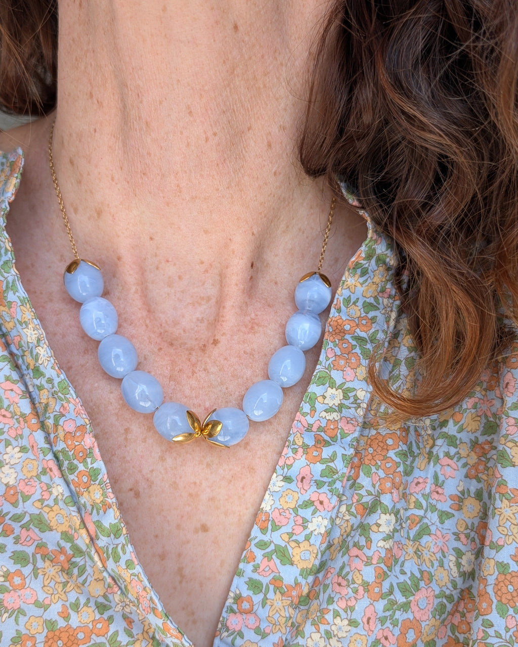 Collier Olivia perle ovale resine bleu azur porté par une femme avec une blouse fleurie. Création artisanale La Tête dans les Nétoiles  