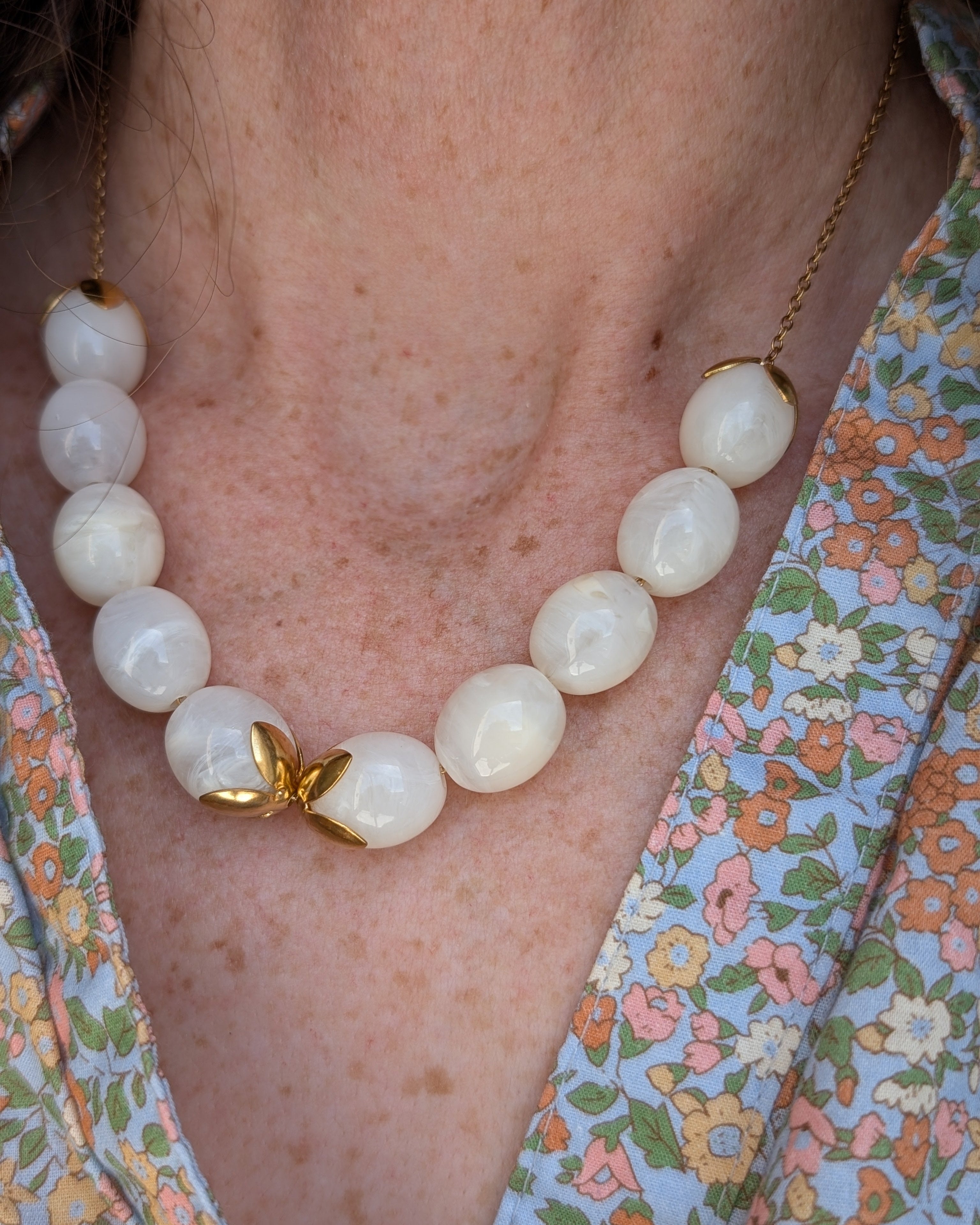 collier Olivia blanc nacré perles résine ovales porté par une femme et blouse fleurie. Créations artisanales La Tête dans les Nétoiles