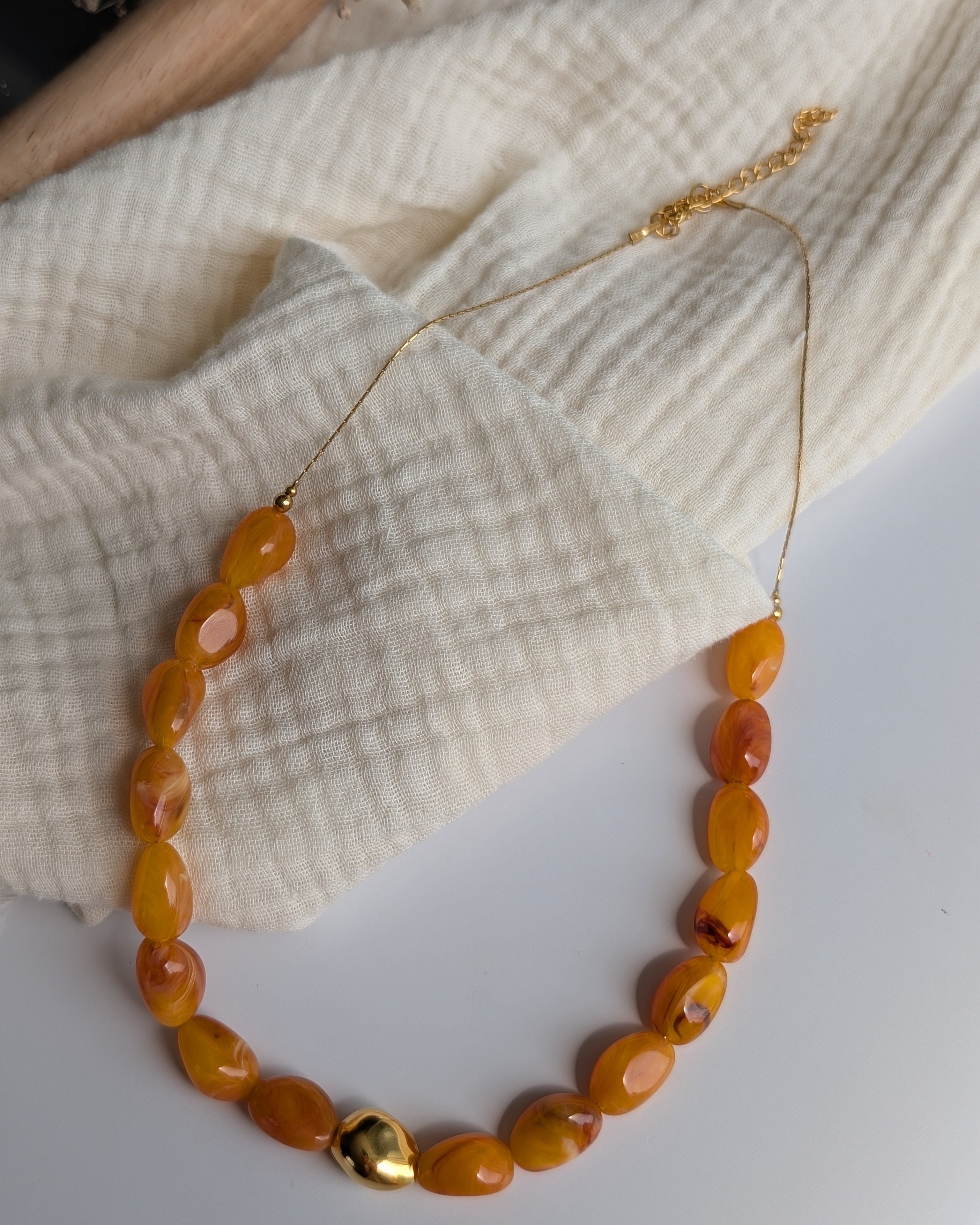 Collier Louison abricot ambré posé à plat sur gaze de coton. Création La Tête dans les nétoiles.