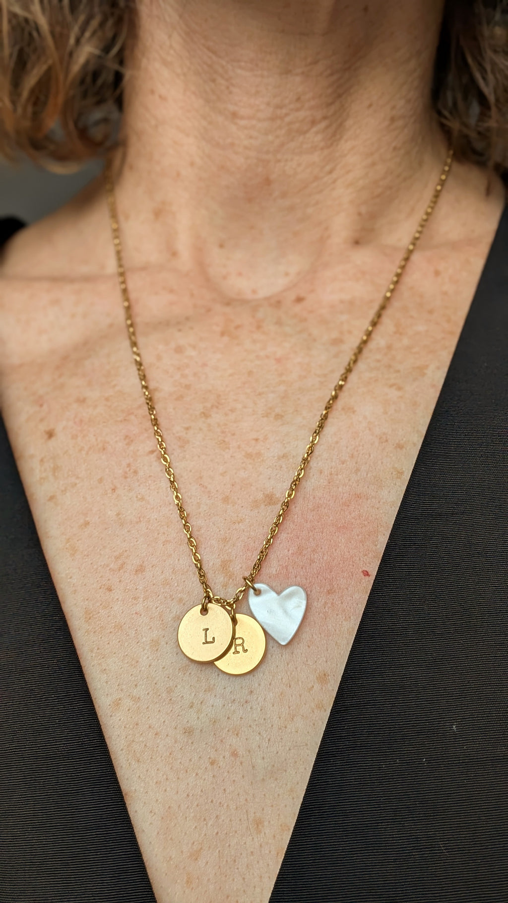 Collier médailles initales estampées à la main avec pendentif coeur blanc nacré porté par une femme. Création artisanale la Tête dans les Nétoiles
