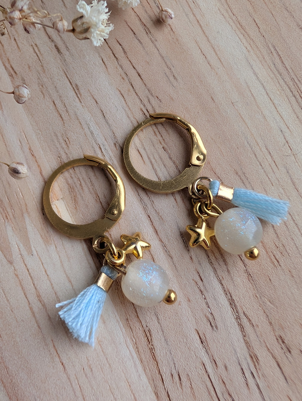 Créole enfant Ma Bonne étoile pompon bleu et paillette bleu sur fond en bois. Créole en acier inoxydable doré. Création La Tête dans les Nétoiles