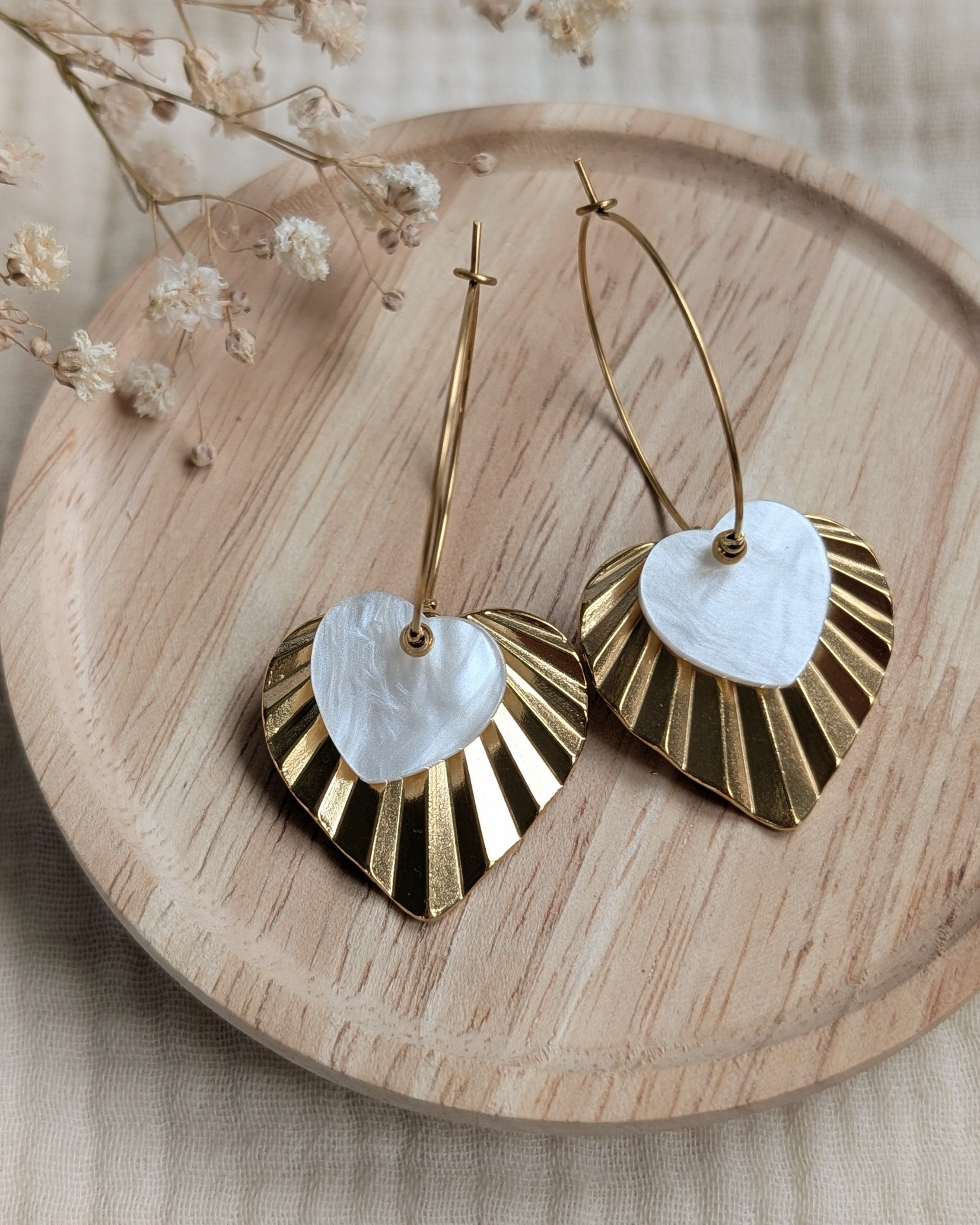 Creoles ALMA blanc nacre coeur en acrylique reflet nacré irisé et coeur strié en acier inoxydable doré. Photo sur support en bois. Création artisanale La Tête dans les Nétoiles
