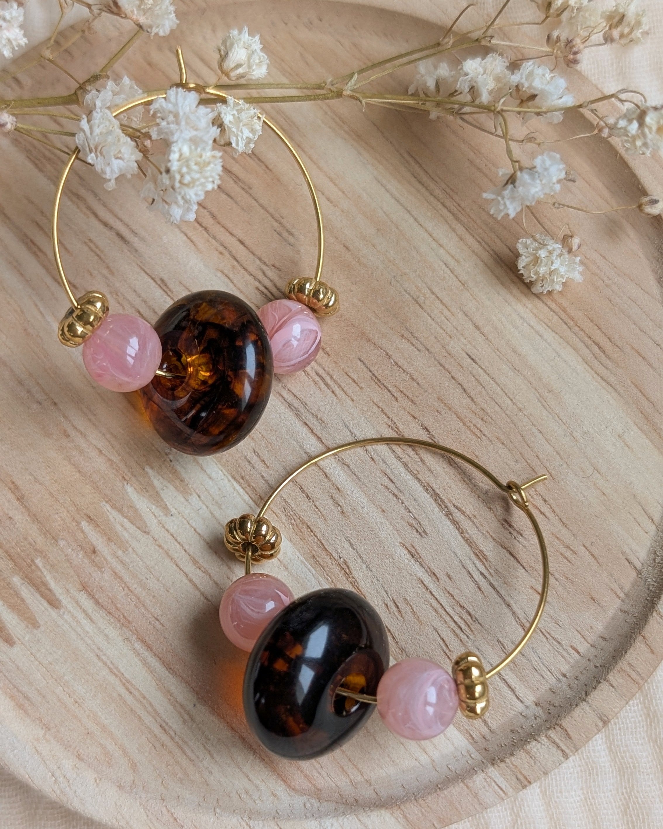 Boucles d'oreilles créoles Elise en acier doré avec perles rose poudré et perle centrale ambre foncé sur support en bois. création artisanale La Tête dans les Nétoiles