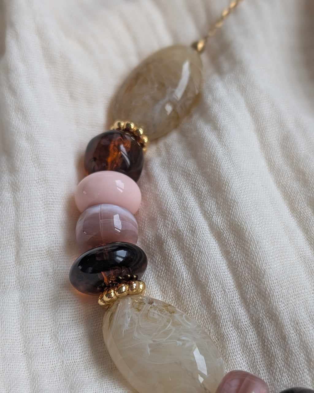 Perles en résine irrégulières aux nuances de rose crème et ambré. perles marbrées enfilées sur une chaîne. détails de perles rondelles dorées en métal design quality. Création artisanale La Tête dans les Nétoiles