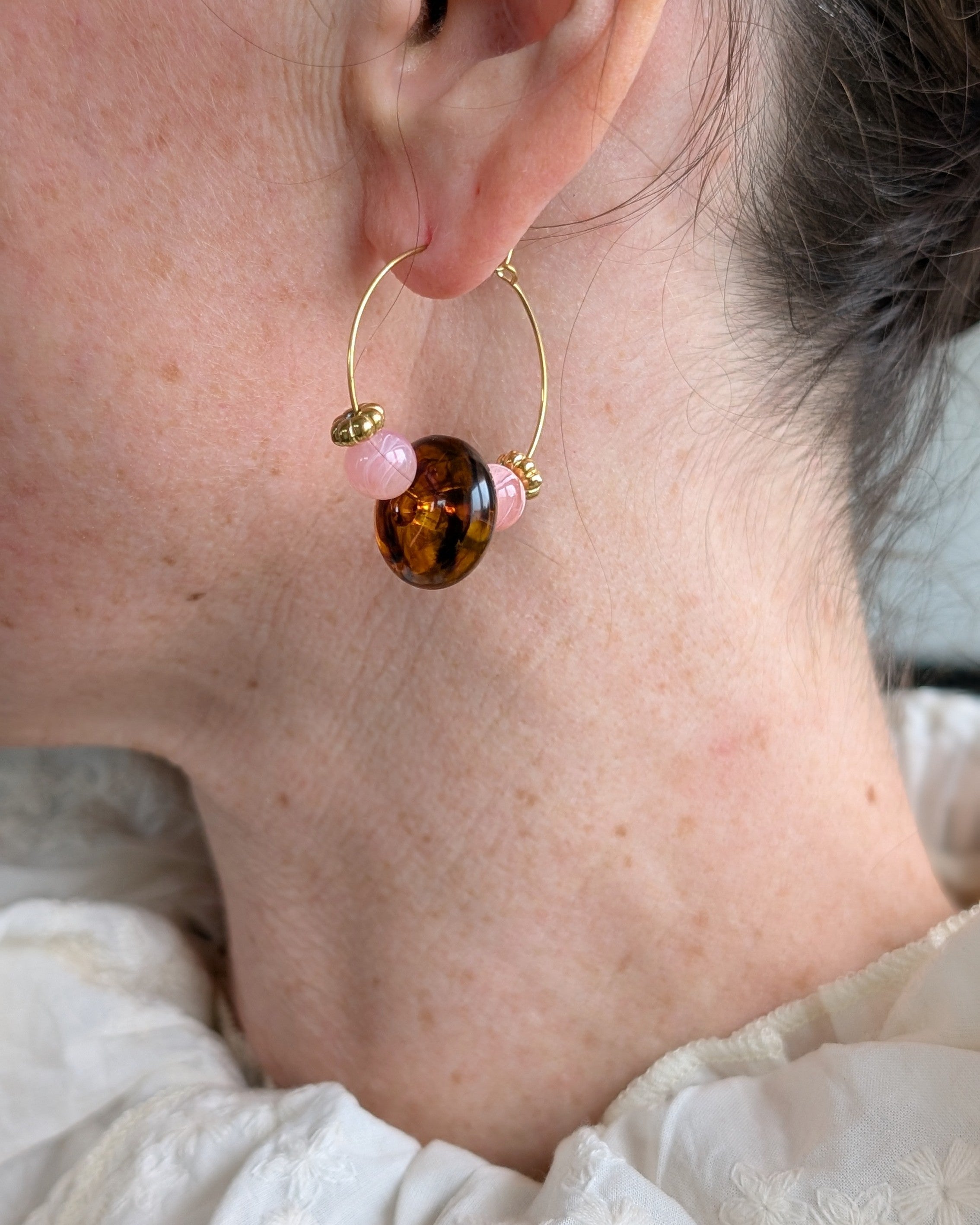 Créole Elise portée avec un chemisier blanc, soulignant le contraste entre le rose quartz et l'ambre fumé. Création artisanale La Tête dans les Nétoiles