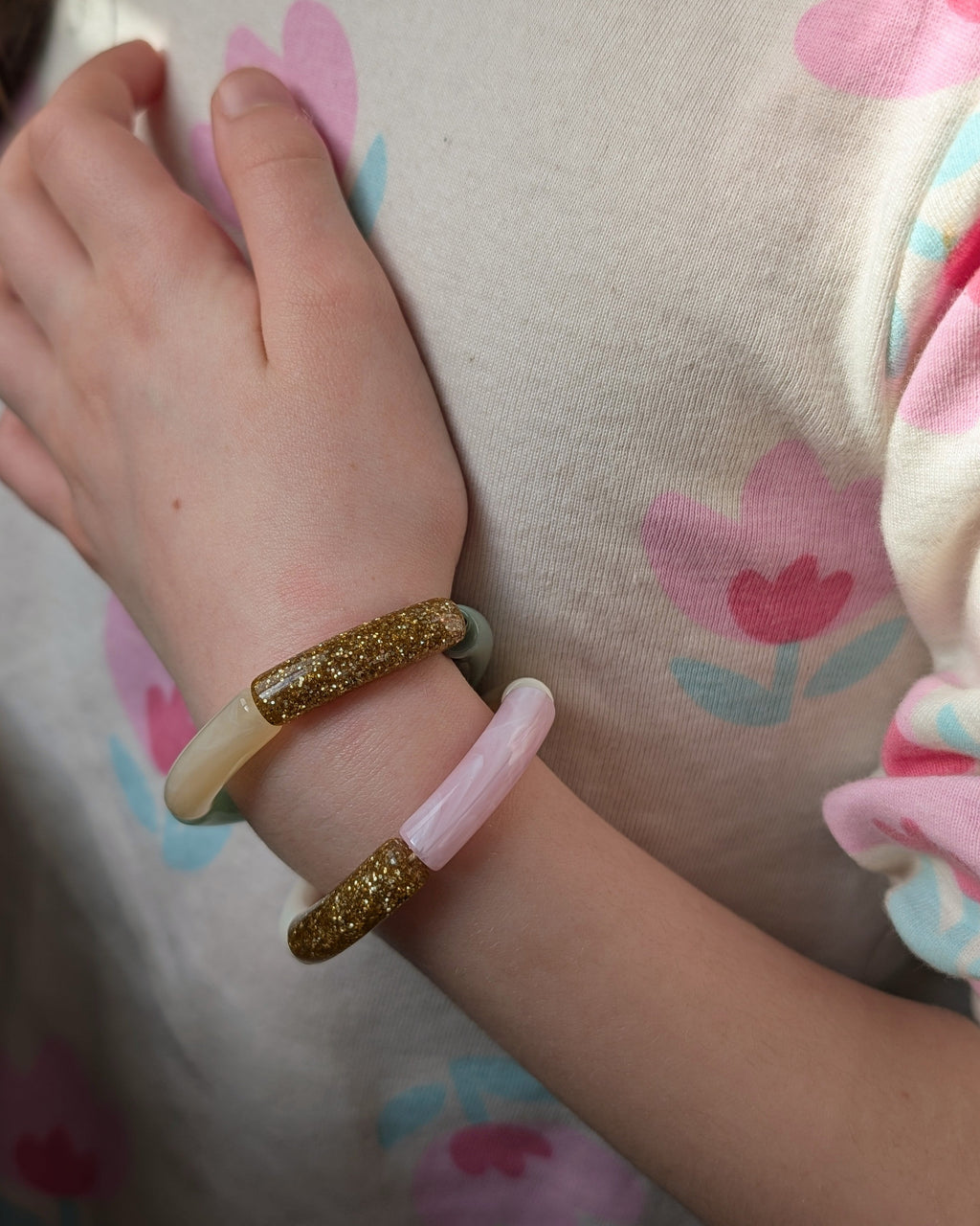 Duo de bracelets perles tube mini taille enfant. Portés par une enfant . Un en vert et un en rose. avec un tee shirt à fleurs