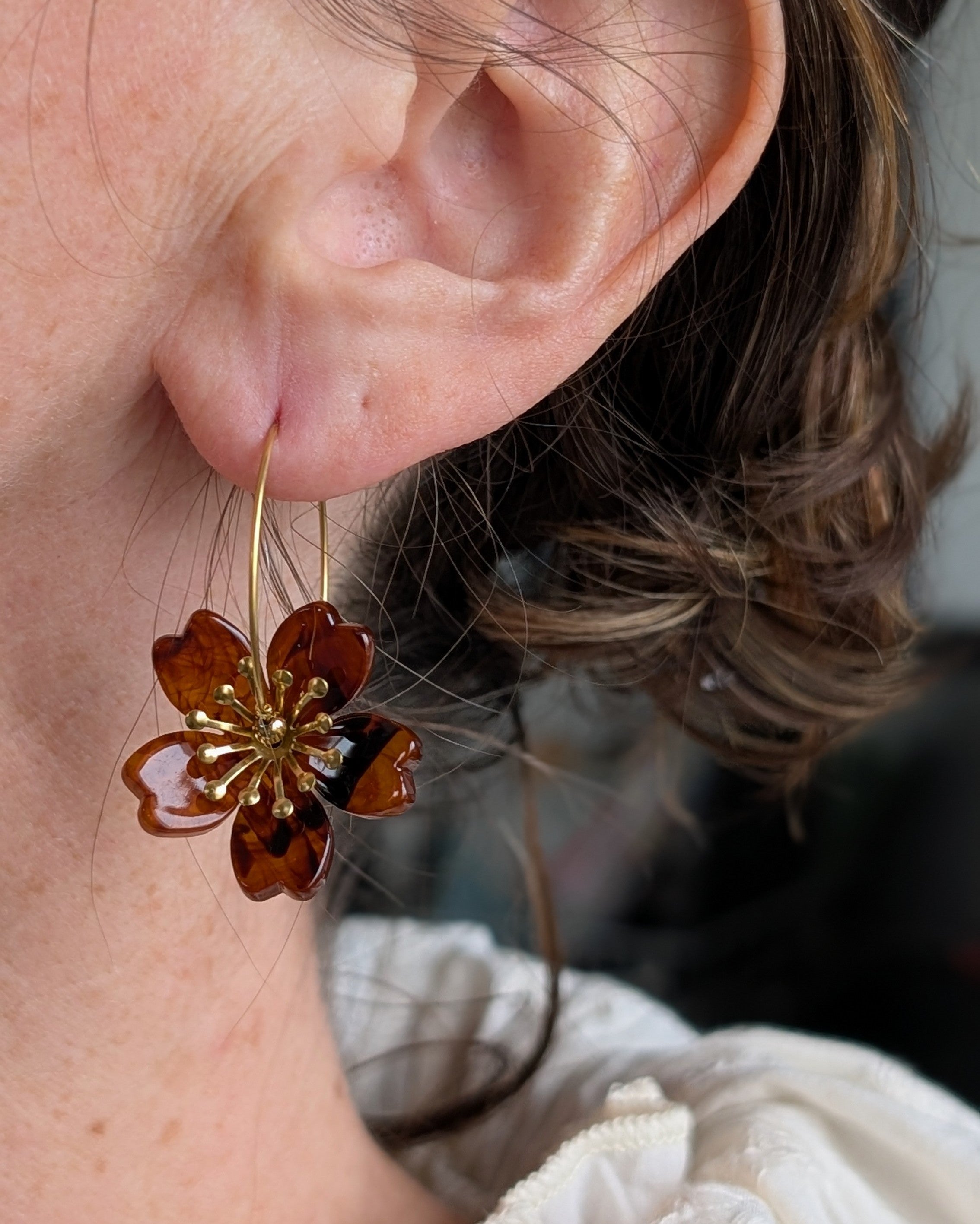 Boucles d'oreilles Siloé ambre foncé portées, design floral aux nuances brunes profondes et pistils dorés. Créoles en acétate de cellulose et acier inoxydable doré. Création artisanale La Tête dans les Nétoiles