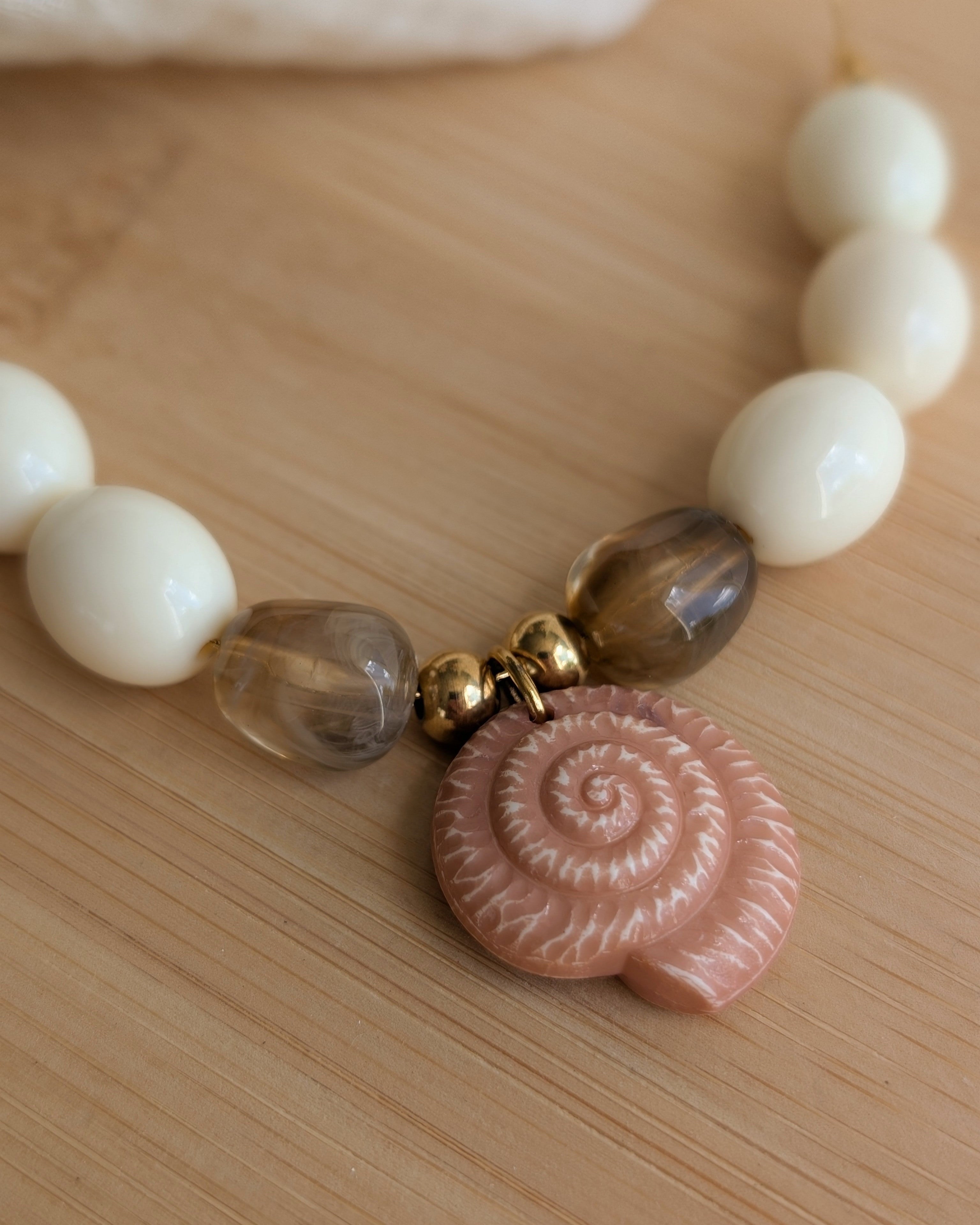 Gros plan sur le pendentif ammonite marron clair et perles olive crème collier Azura. Création artisanale La Tête dans les Nétoiles 