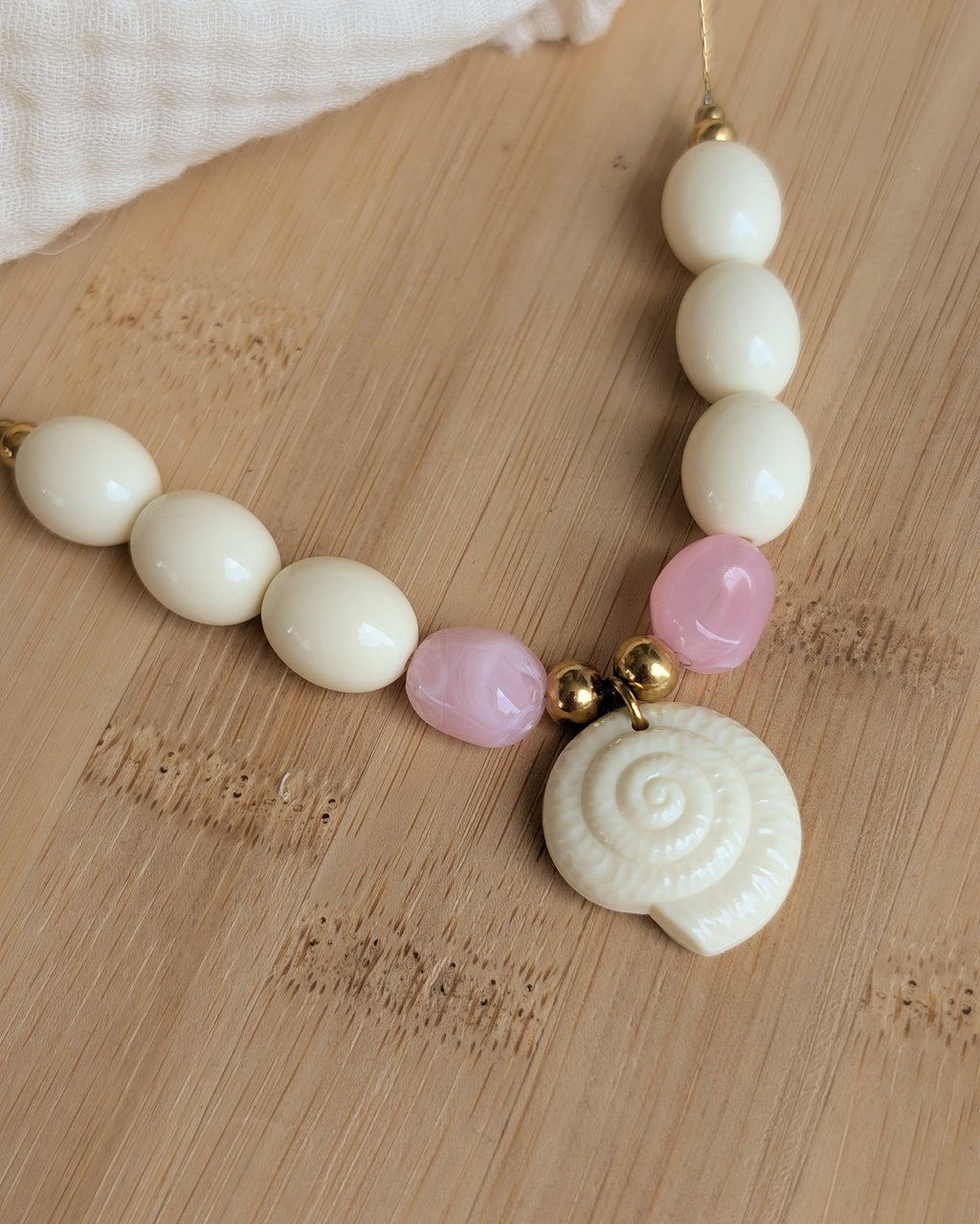 Gros plan sur les perles et pendentif coquillage du collier Azura en résine . Posé sur plateau en bois. Création artisanale La Tête dans les Nétoiles 