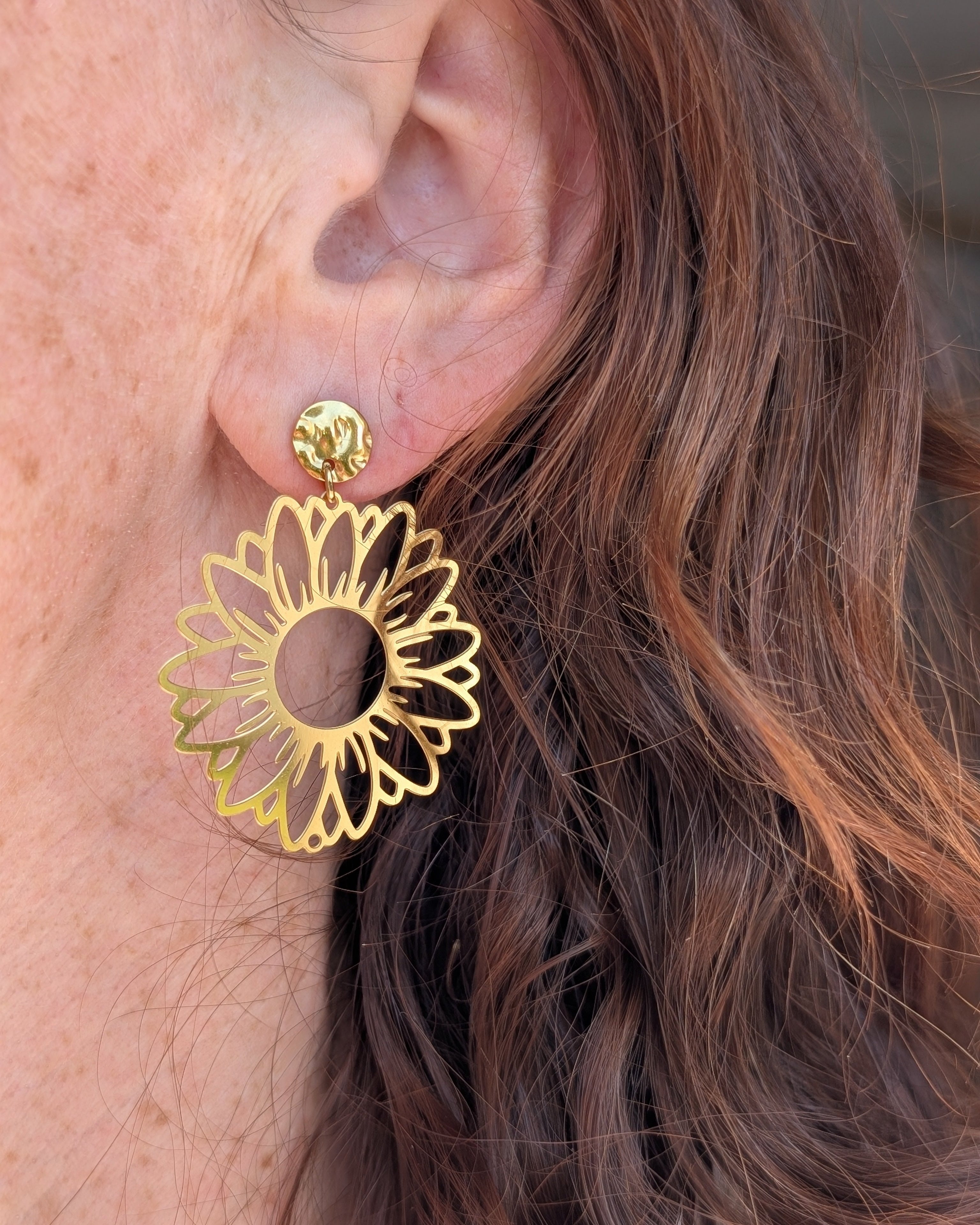 Boucles d'oreilles maxi tournesol Elia en acier inoxydable doré. Portées par une  femme. Créations artisanales La Tête dans les Nétoiles