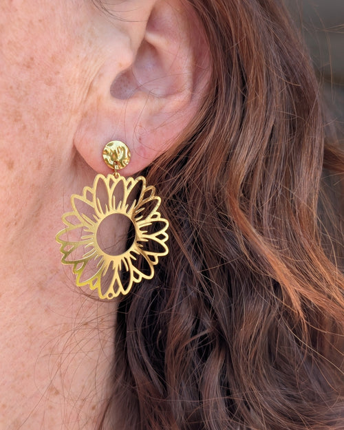 Boucles d'oreilles maxi tournesol Elia en acier inoxydable doré. Portées par une  femme. Créations artisanales La Tête dans les Nétoiles