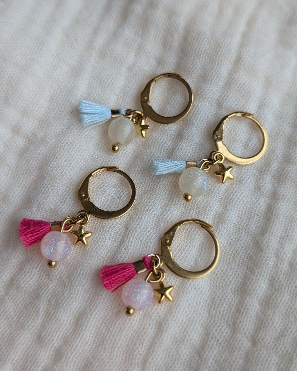 Paires de créoles enfant bleu ciel et rose magenta avec étoile dorée et pompon. Créole en acier inoxydable Création artisanale La Tête dans les Nétoiles.