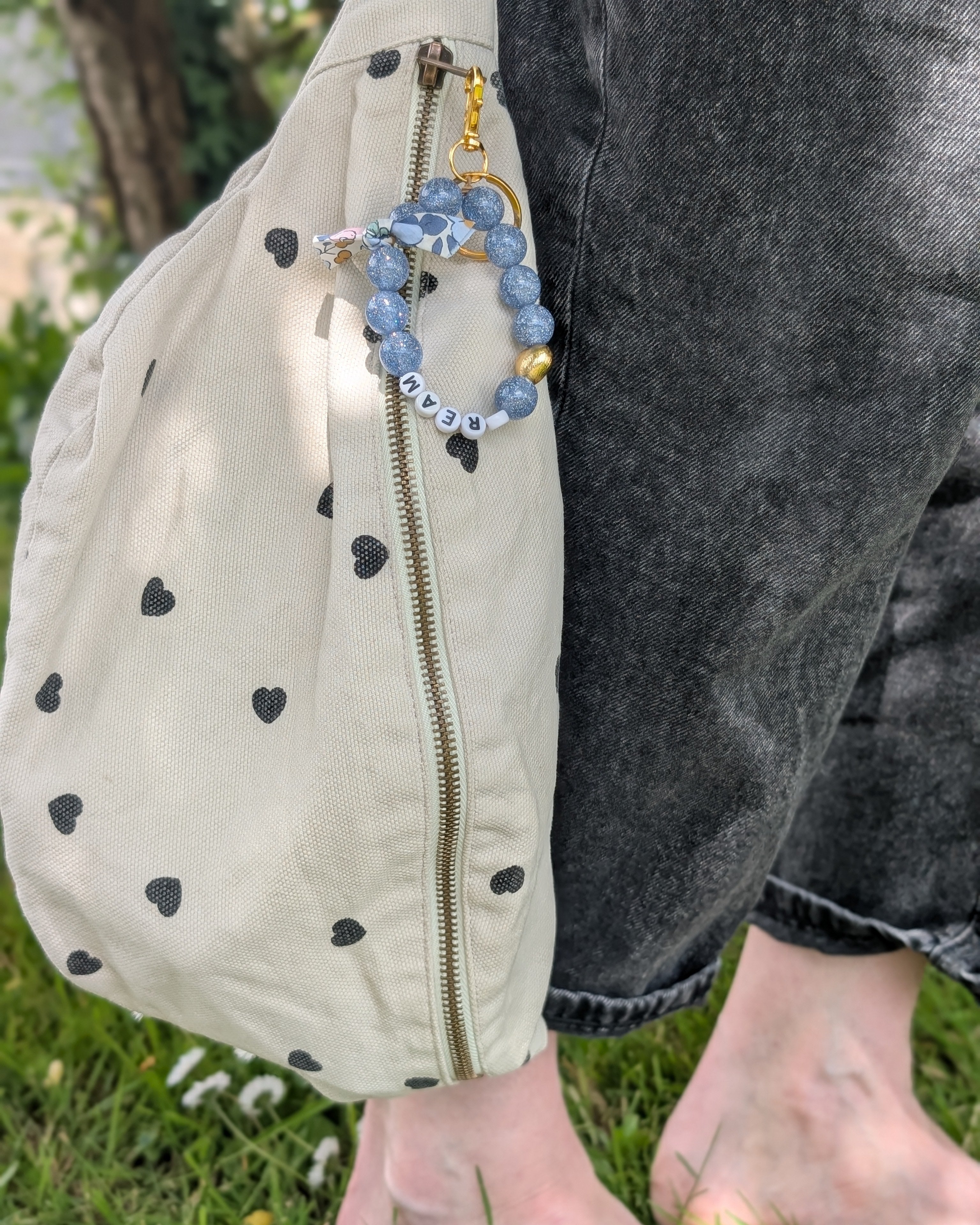 Porte clés et bijoux de sac liberty glowy bleu ciel paillettes et mot dream accroché à un sac banane. Créations artisanales La Tête dans les Nétoiles