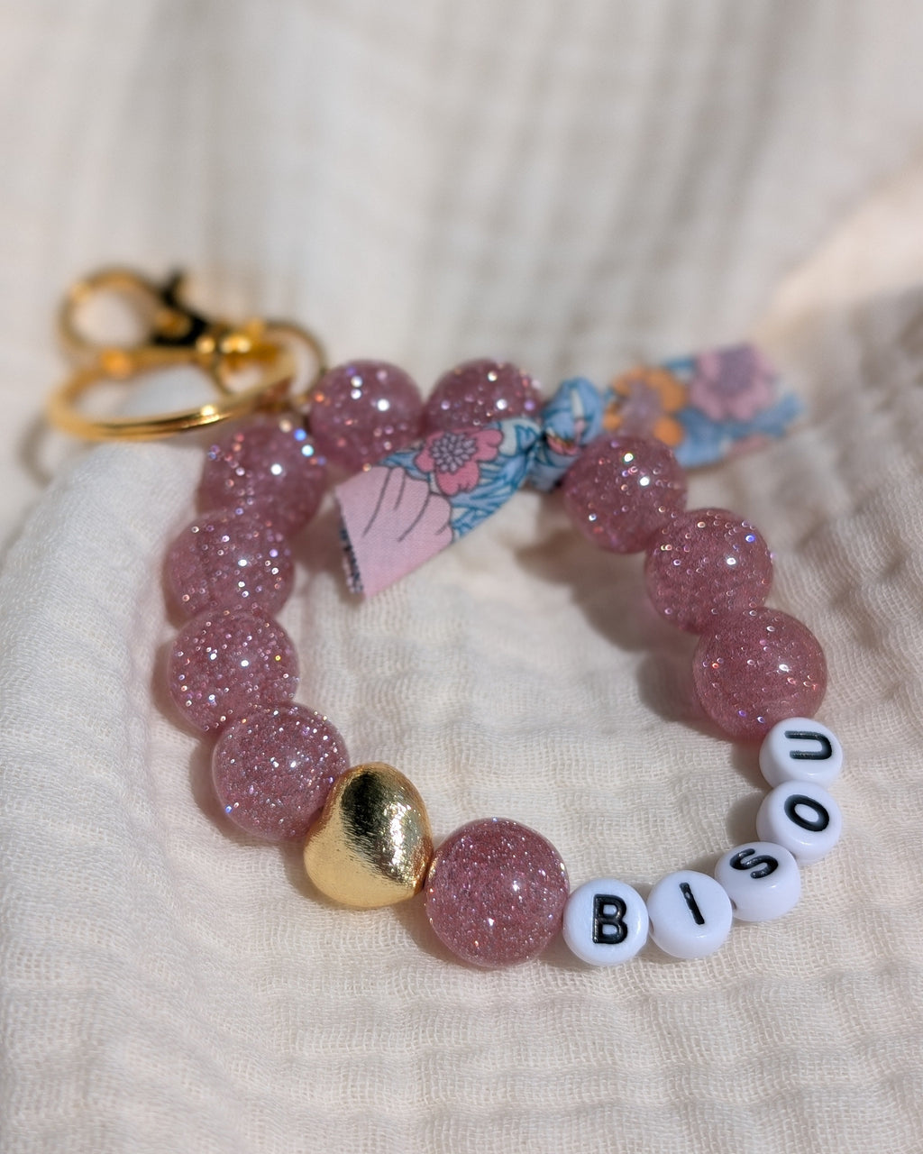 Porte clés et bijoux de sac liberty glowy vieux rose paillettes posé sur gaze de coton. Mot bisou à personnaliser. Créations artisanales La Tête dans les Nétoiles