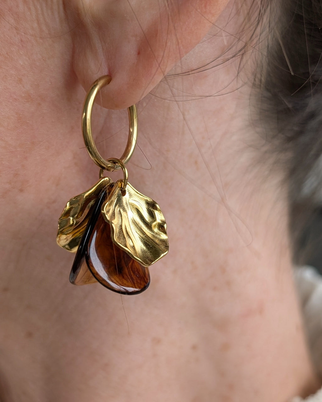 Boucles d'oreilles créoles Sora coloris ambre foncé portées, bijou de créateur artisanal avec feuilles dorées texturées. Création La Tête dans les Nétoiles