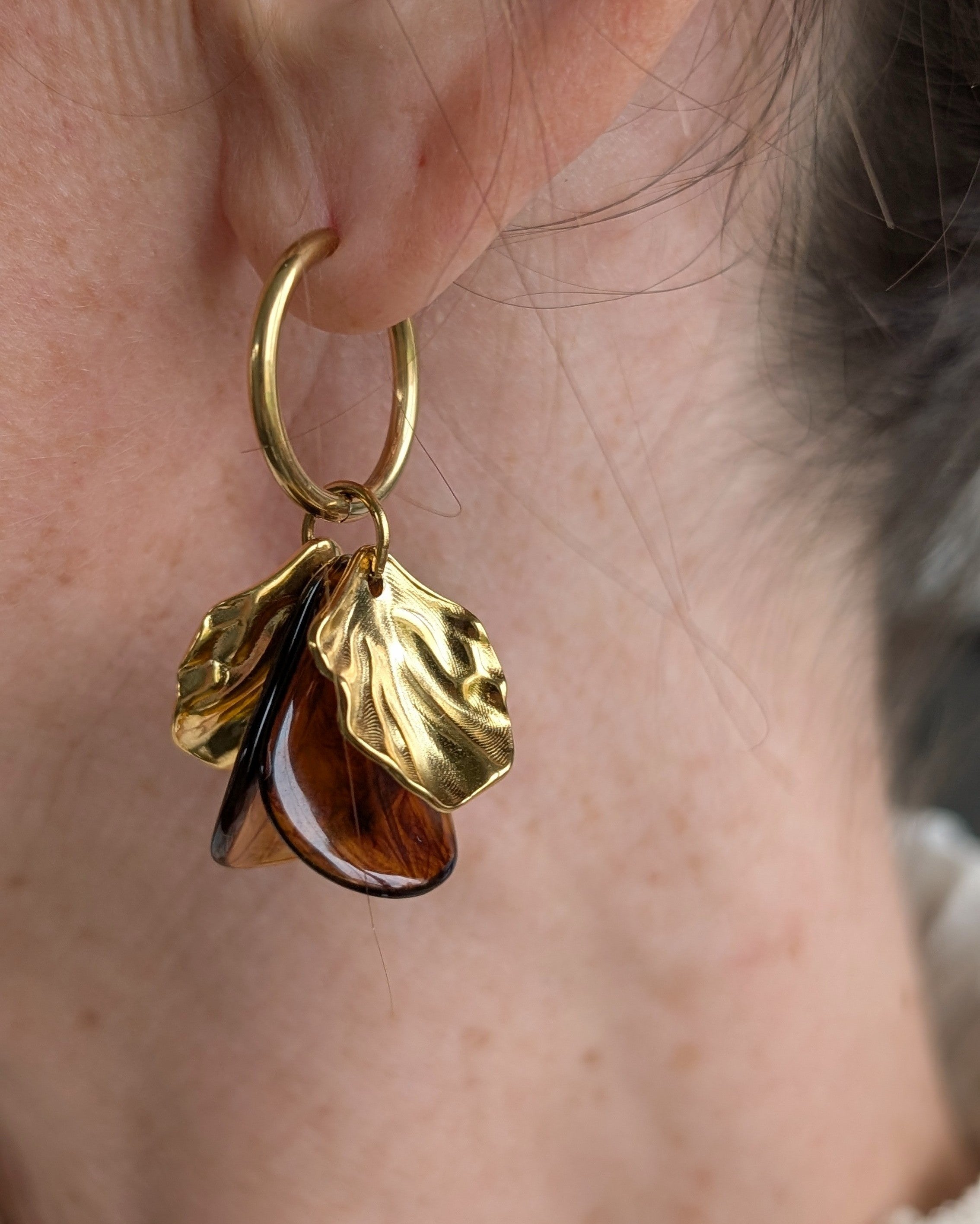 Boucles d'oreilles créoles Sora coloris ambre foncé portées, bijou de créateur artisanal avec feuilles dorées texturées. Création La Tête dans les Nétoiles
