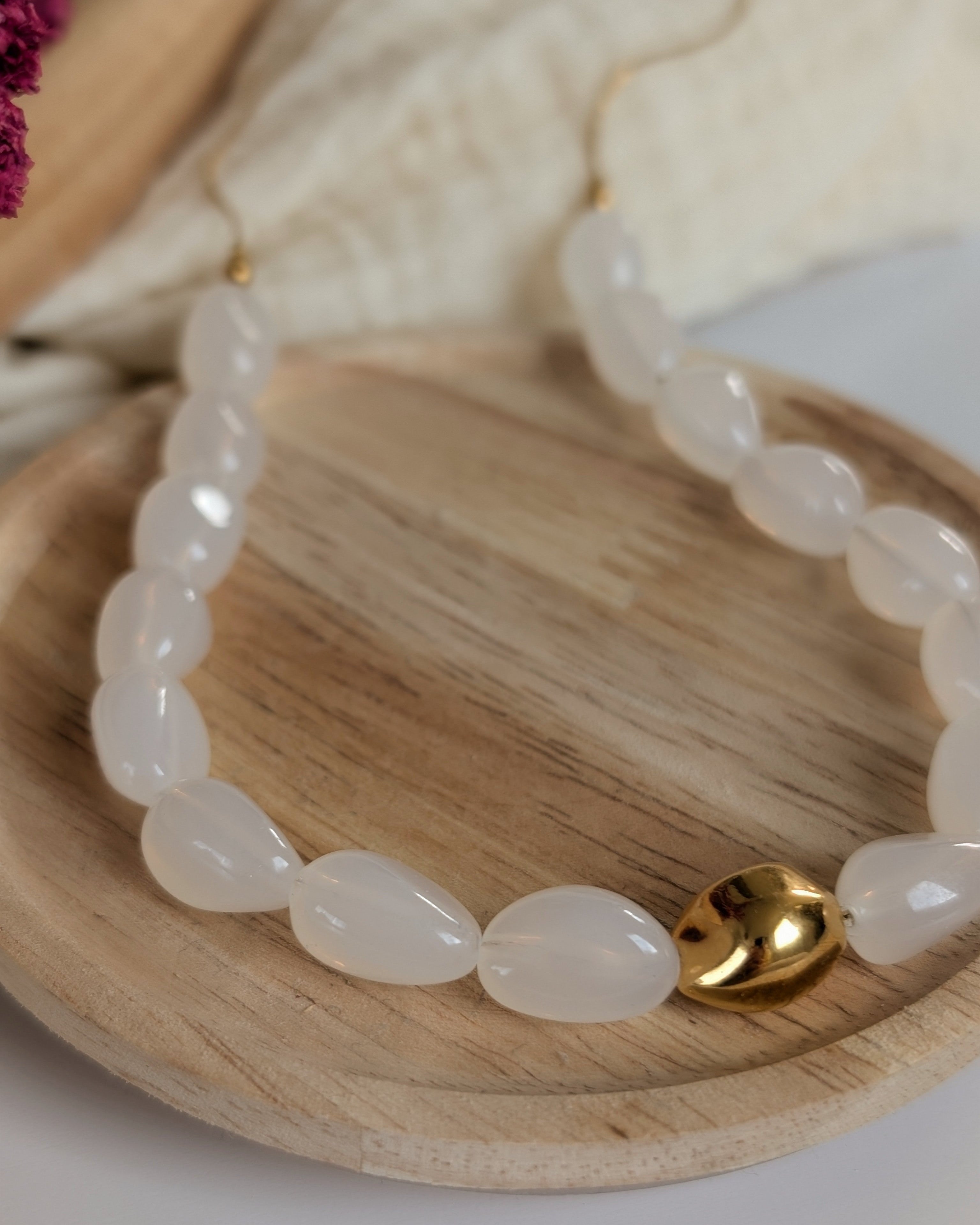 Gros plan sur le collier Louison coloris blanc opale gros plan sur la perle doré. Posée à plat sur rondin de bois. Créations fait main La Tête dans les Nétoiles