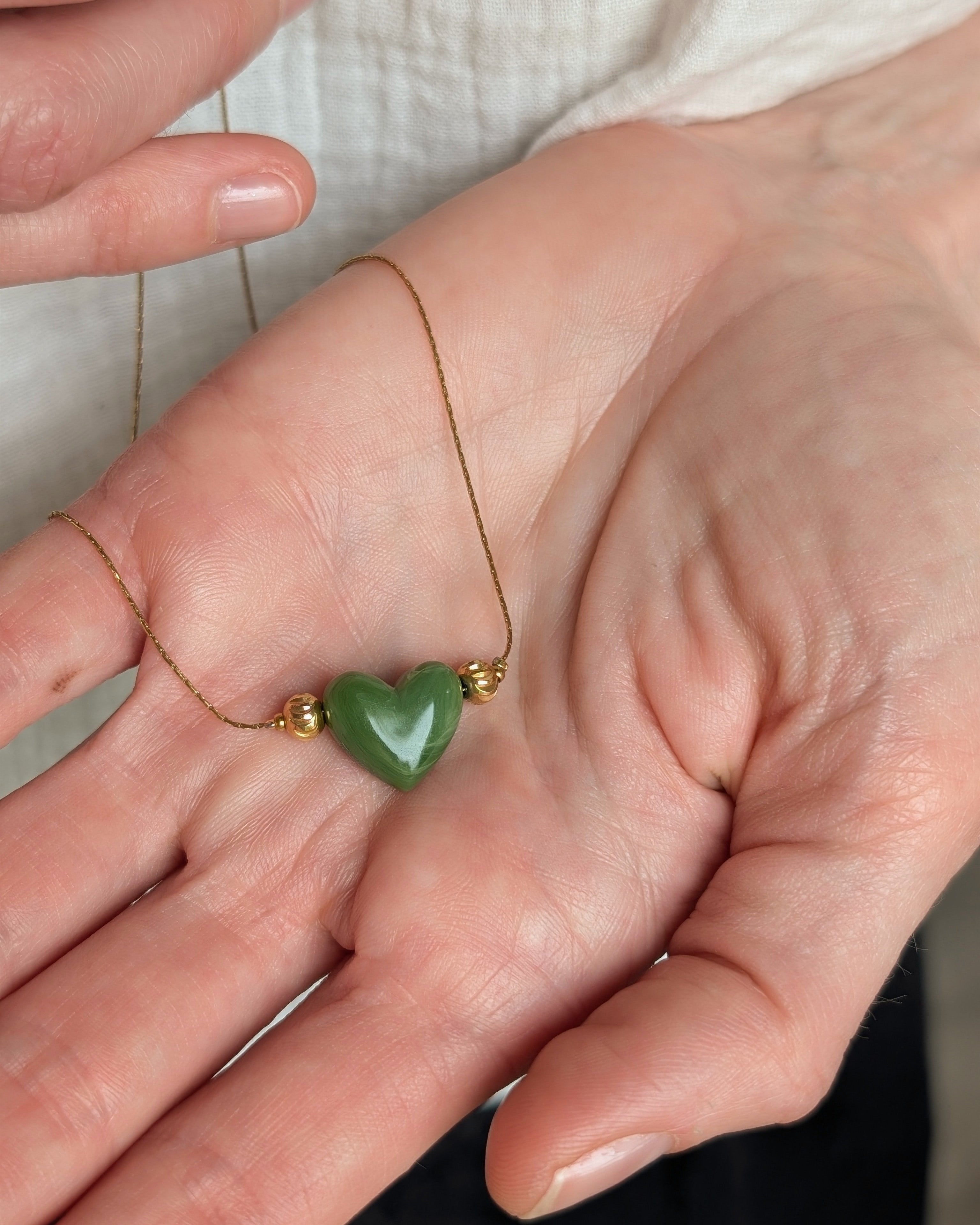 Gros plan du pendentif coeur marbré vert en résine dans la main d'un femme. 