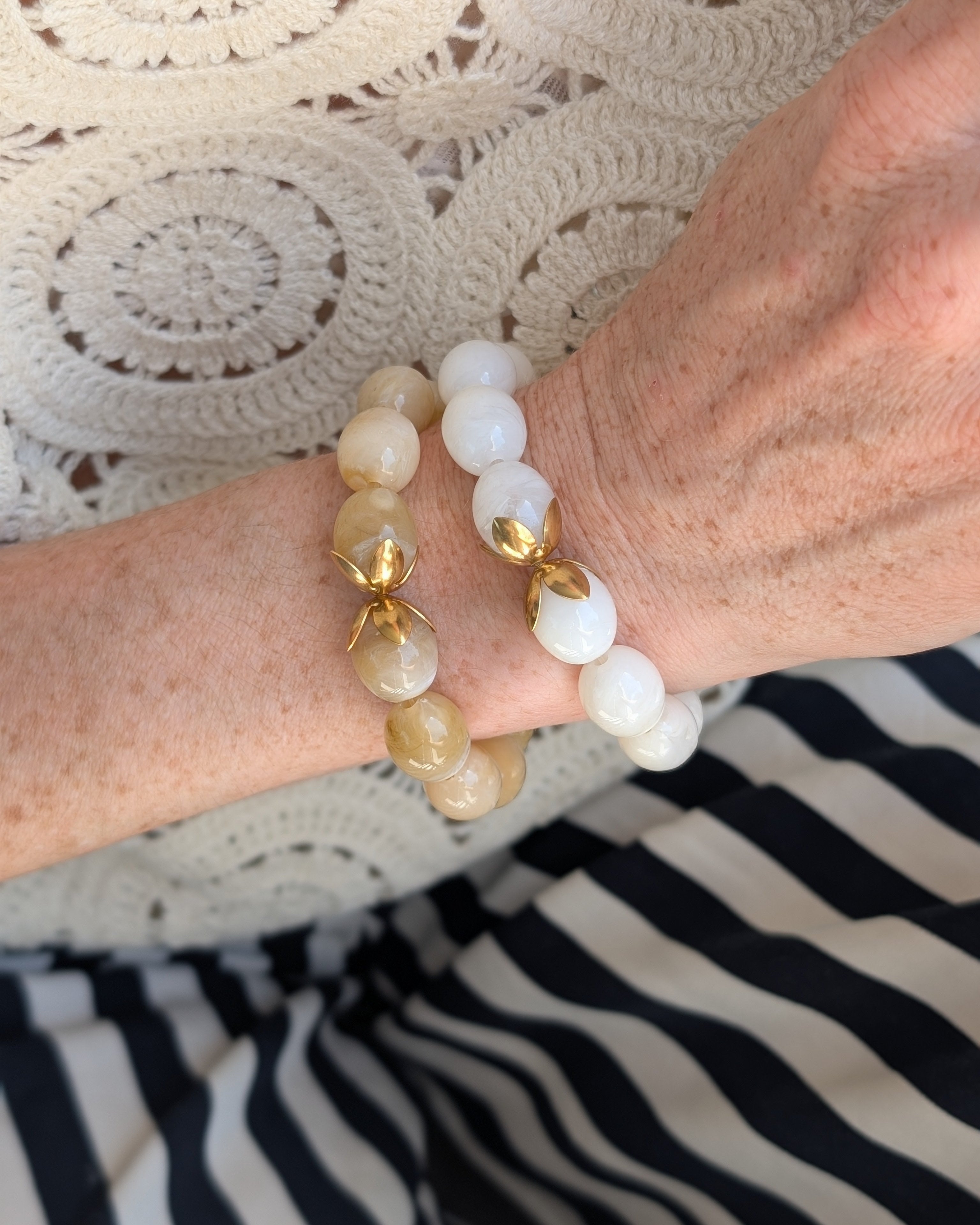 Accumulation de bracelets Olivia un en blanc et un en beige en résine marbrées. Portés au poignet d'une femme. avec un haut brodé. Créations artisanales La Tête dans les Nétoiles