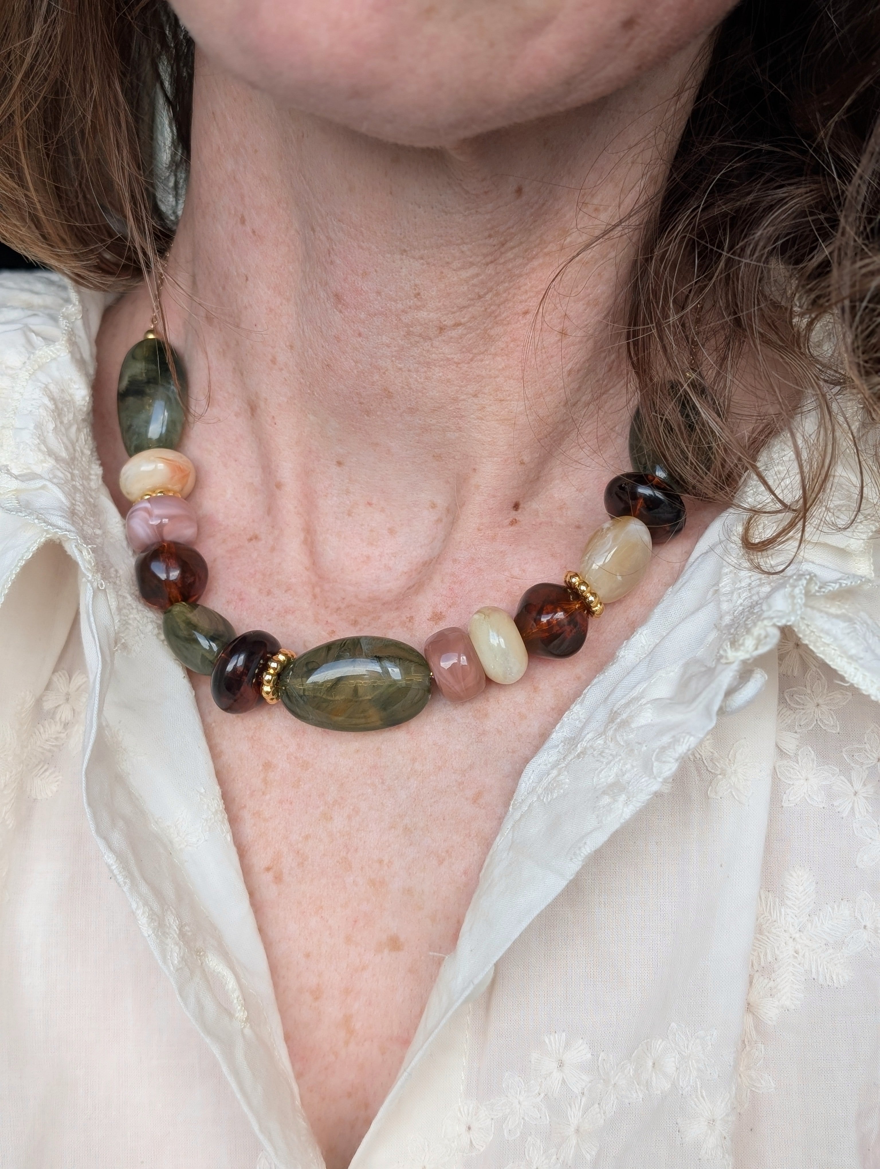 Collier GABIE porté par une femme. Perles irrégulières en résine aux nuances de vert et d'ambre . Création artisanale La Tête dans les Nétoiles