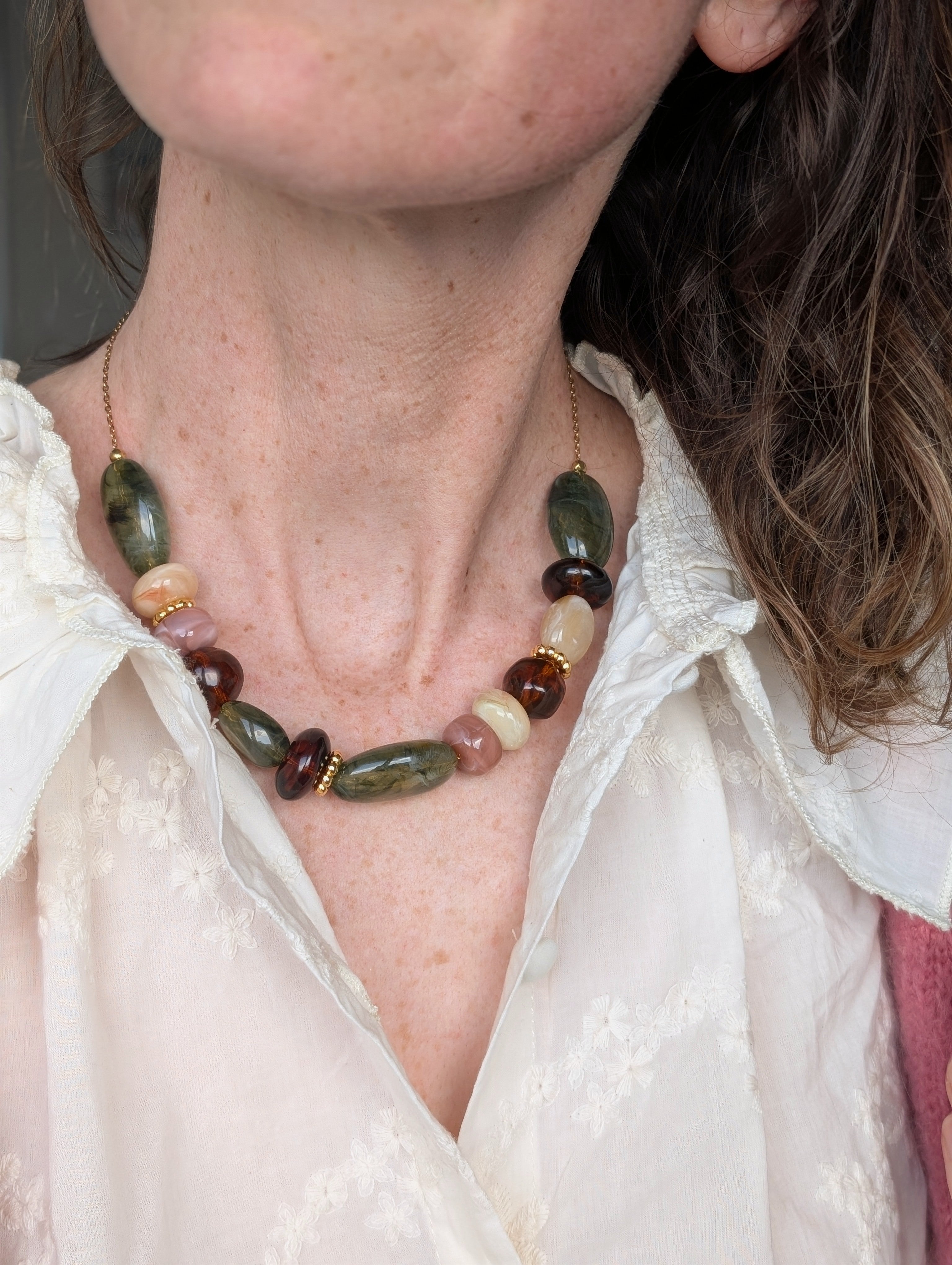 collier GABIE nuances de vert et d'ambre sur fond de gaze de coton. Perles en résine irrégulières enfilées sur chaîne maille forçat. Porté par une femme . Création artisanale La Tête dans les Nétoiles