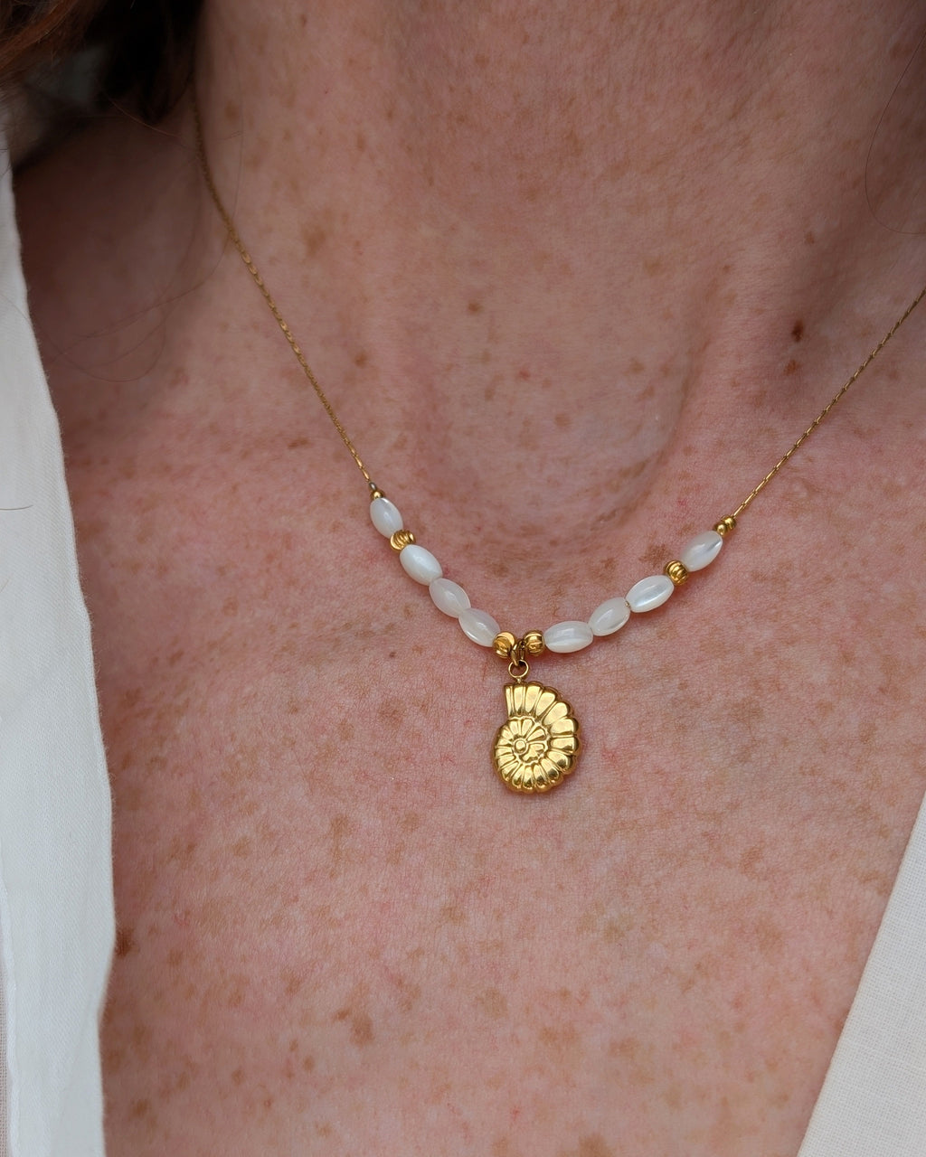 collier Néri pendentif ammonite en acier inoxydable doré porté par une femme. Créations artisanales La Tête dans les Nétoiles 