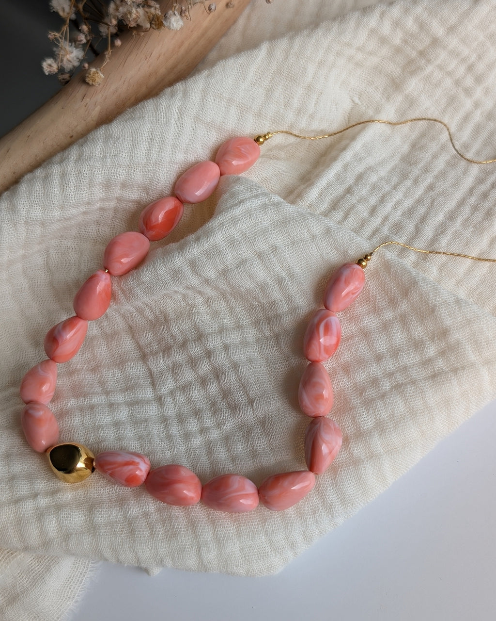 Collier Louison rose corail marbré posé sur gaze de coton. Création La Tête dans les nétoiles
