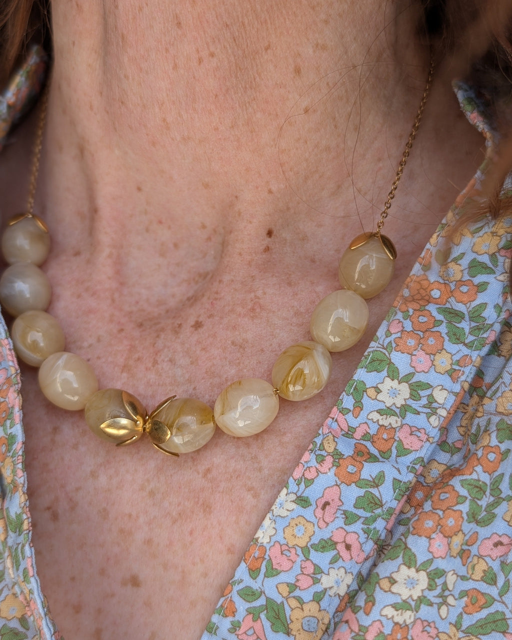 Collier Olivia coloris beige marbré porté par une femme sur blouse fleurie. Créations artisanales La Tête dans les Netoiles