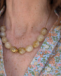 Collier Olivia coloris beige marbré porté par une femme sur blouse fleurie. Créations artisanales La Tête dans les Netoiles