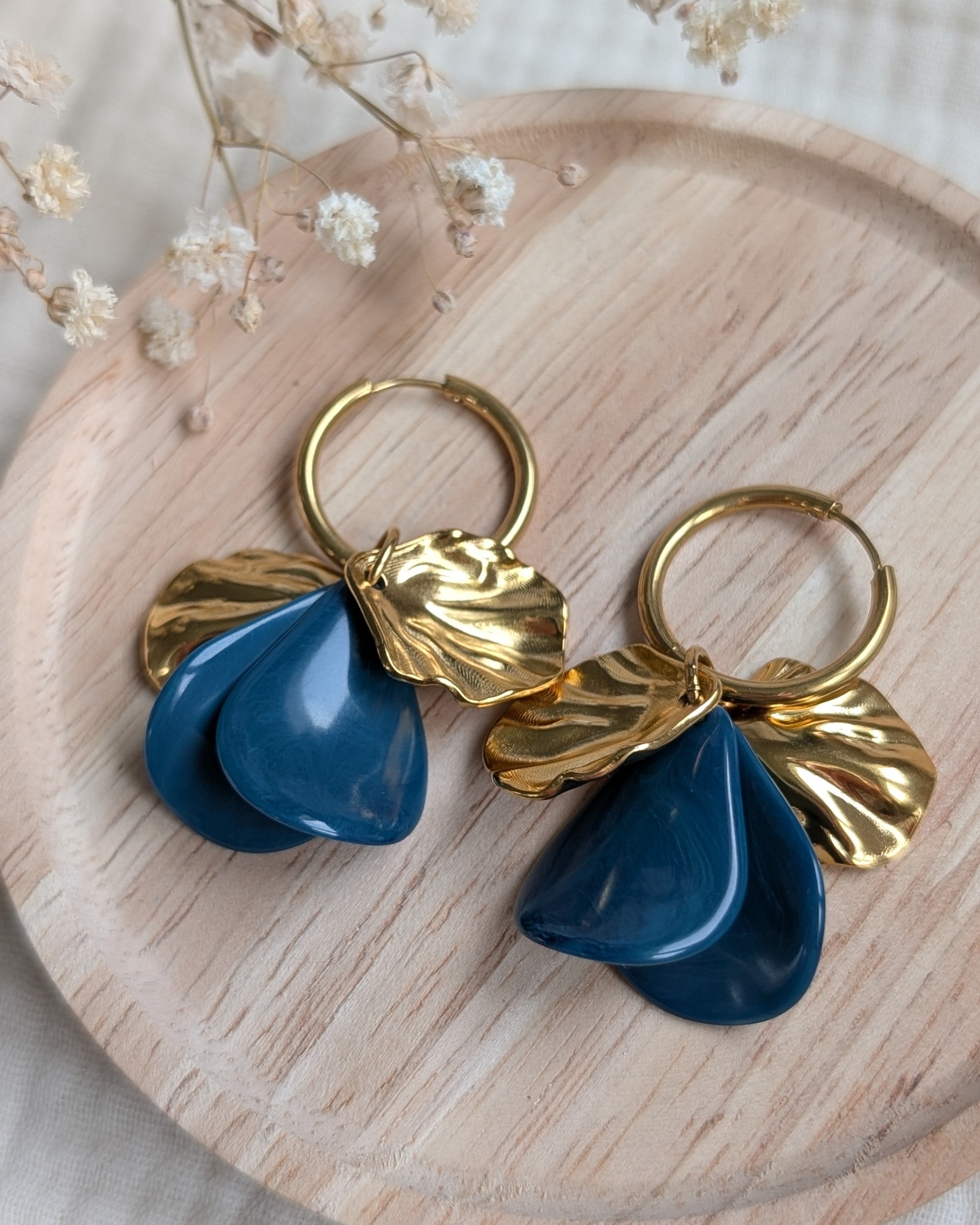 Détail des boucles d'oreilles Sora bleues et dorées sur plateau en bois, bijoux de créateur La Tête dans les N'étoiles.