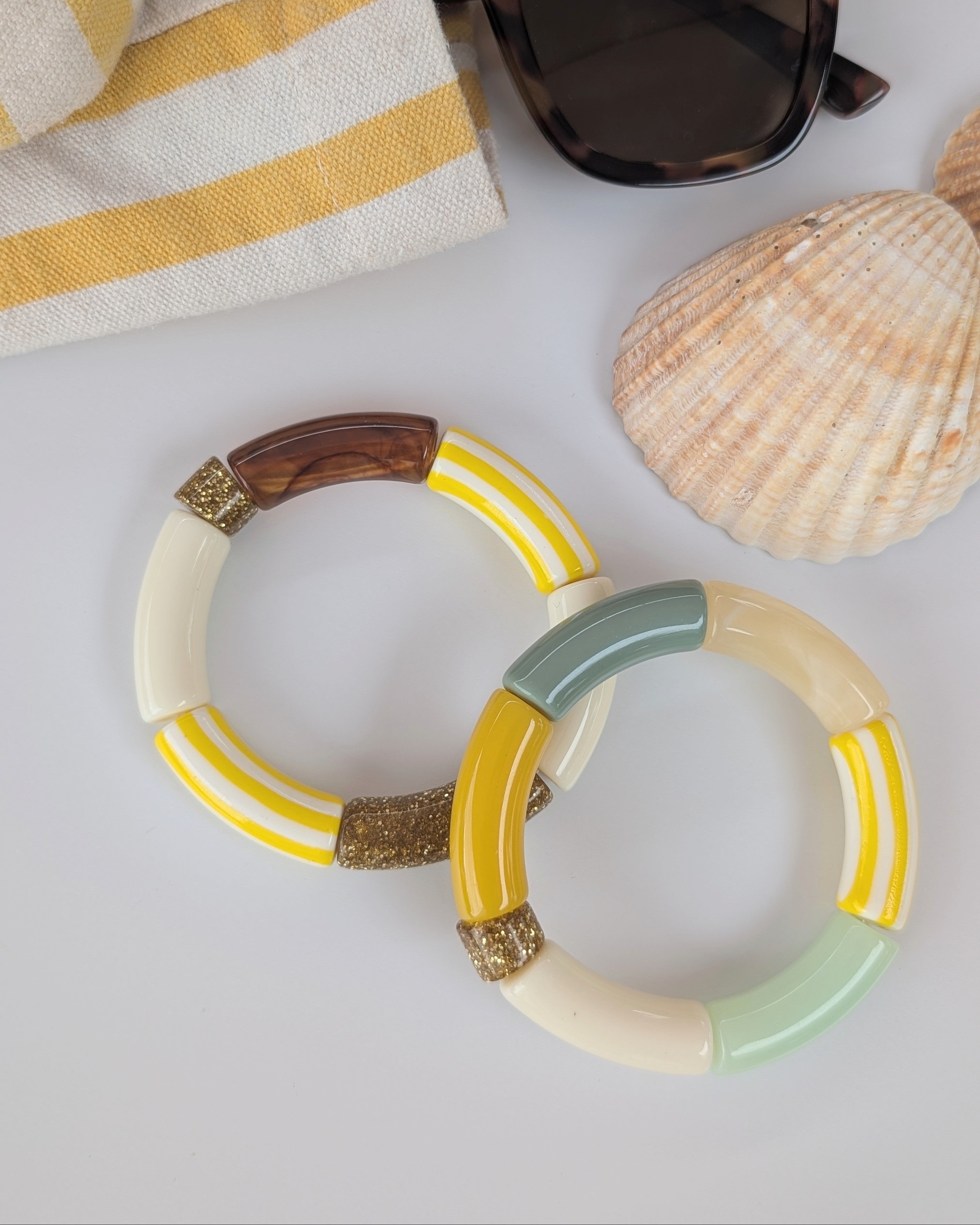 duo de bracelets perles tube à rayures jaune vert glitter paillettes. Posés sur table avec coquillage. Créations Artisanales La Tête dans les Nétoiles.