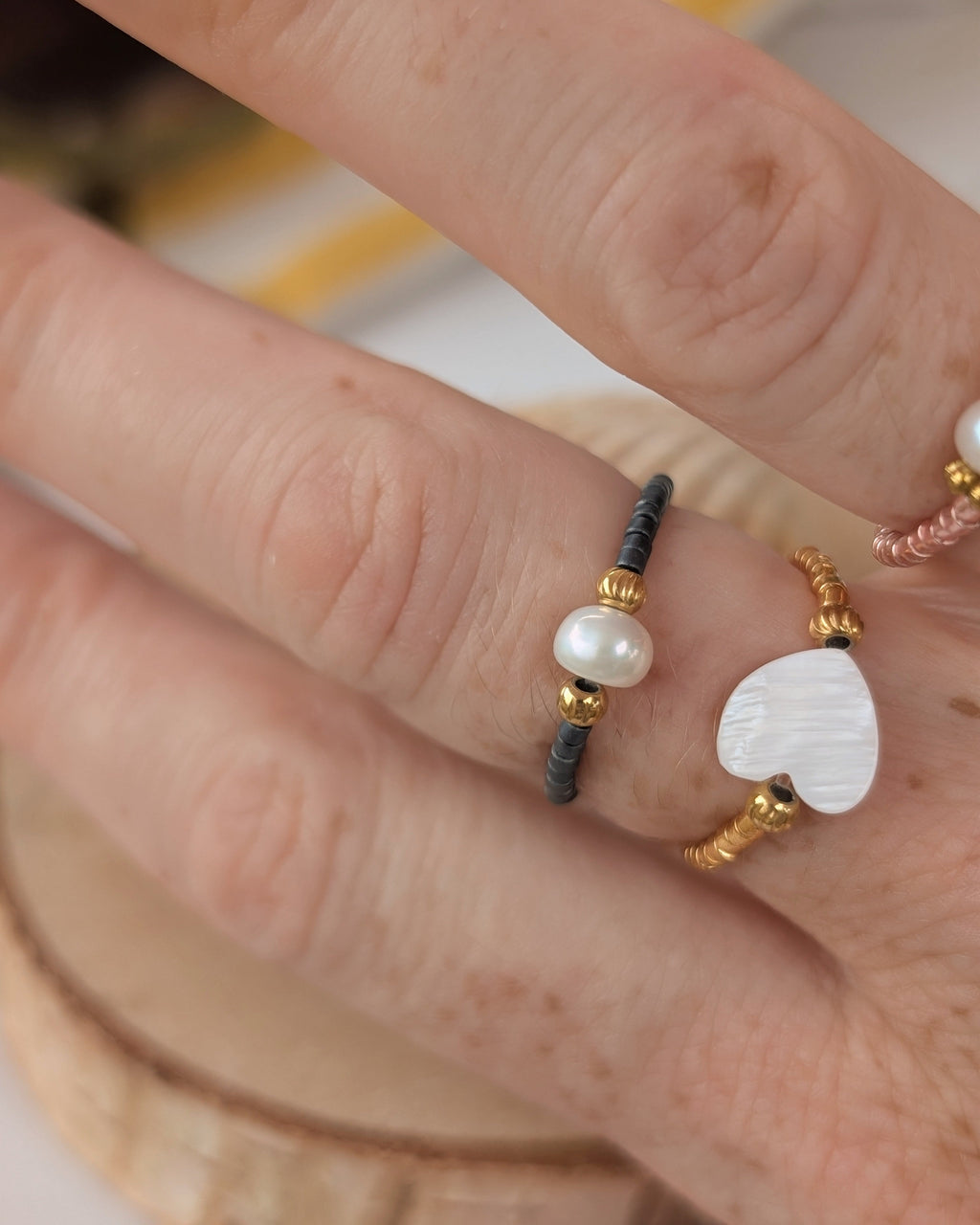 duos de bagues élastiques fait main La Tête dans les Nétoiles. Portées par une femme. Une bague bleu grise avec perle d'eau douce ronde et perle maxi coeur nacre et perles miyuki doré.