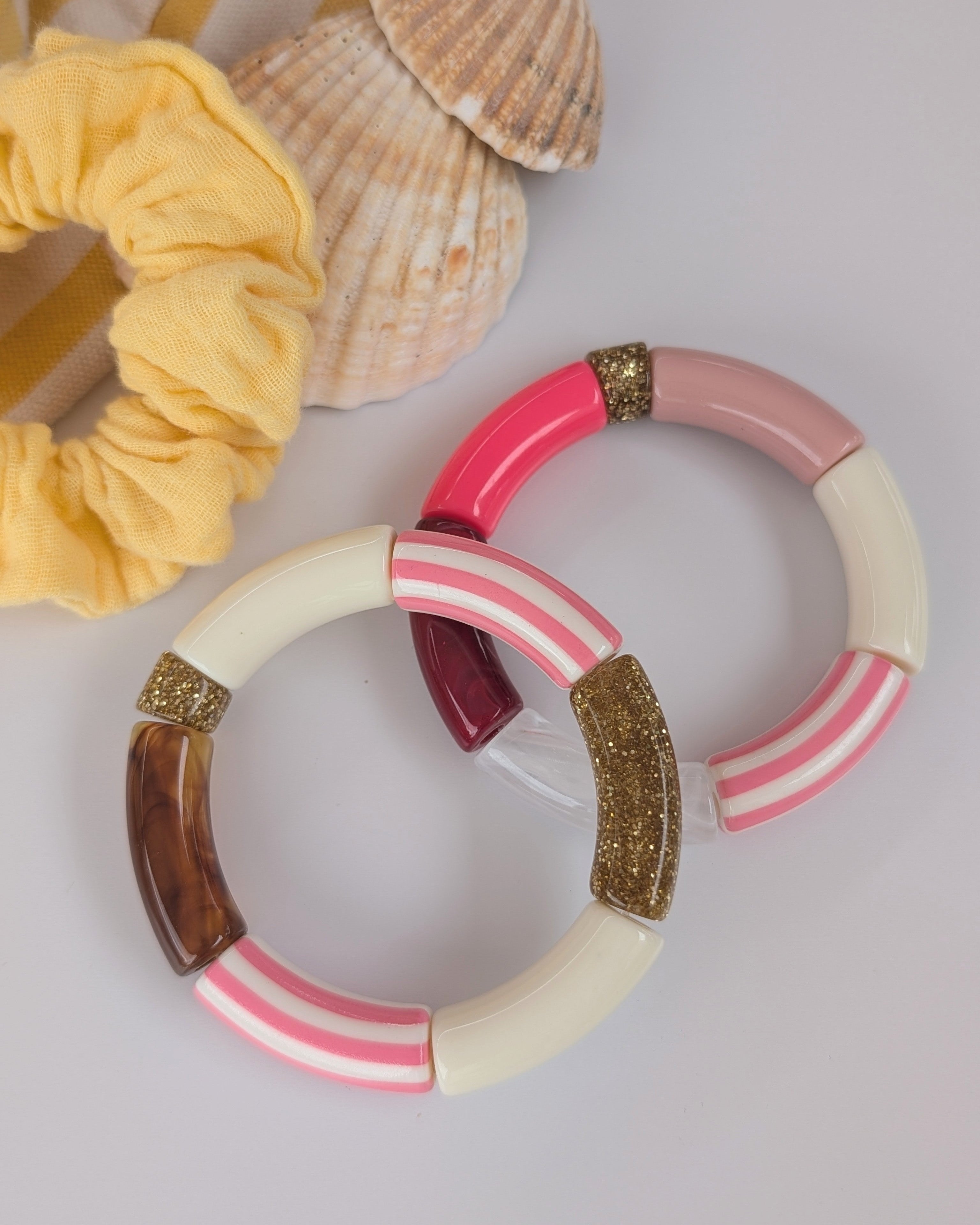 Duos de bracelets perles tube à rayures rose posés sur table. Mise en avant du coloris rose et glitter doré. Création artisanales La Tête dans les Nétoiles