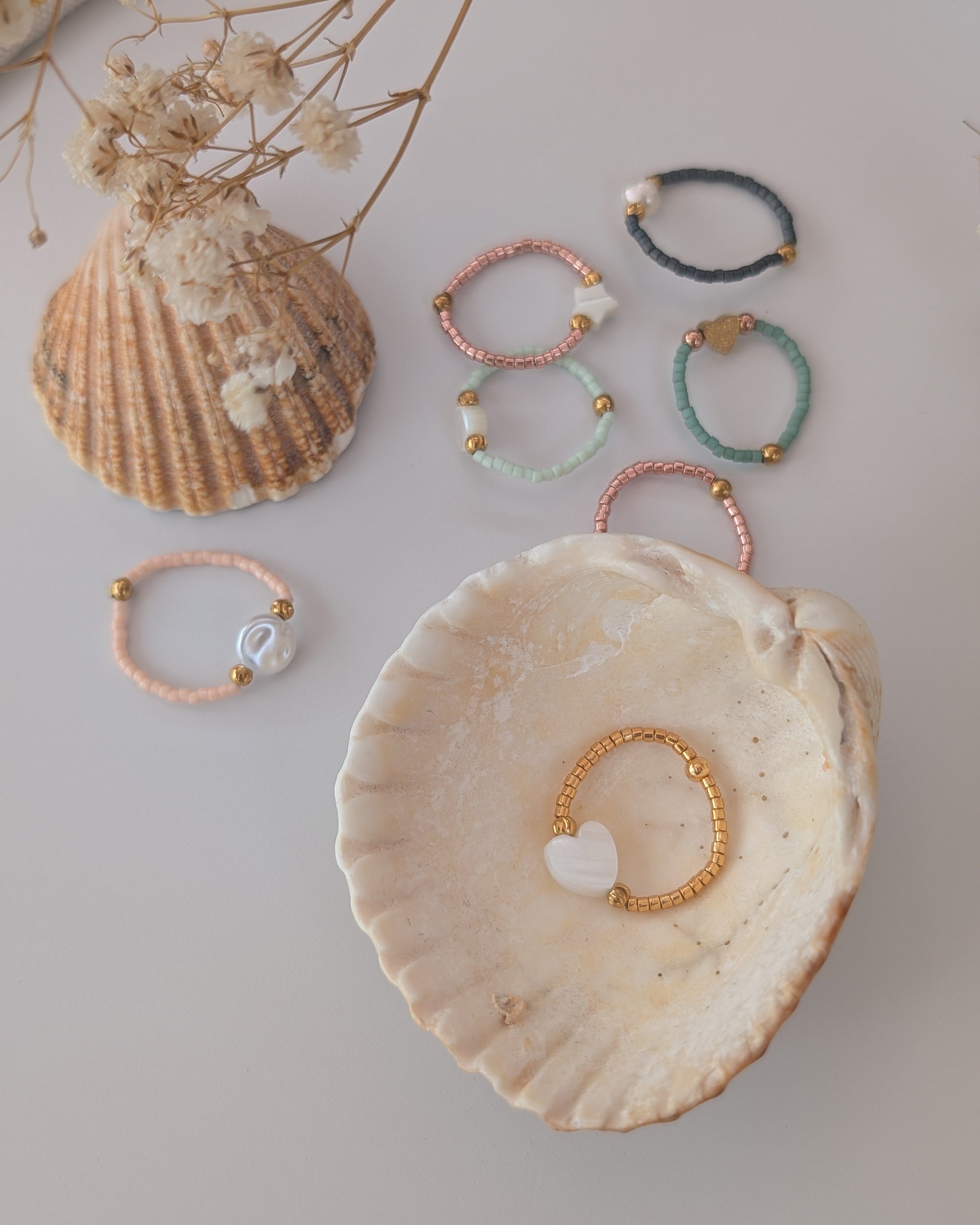ensemble de bagues perles miyuki et nacre, et perles de culture. Posées sur des coquillages. Créations artisanales La Tête dans les Nétoiles