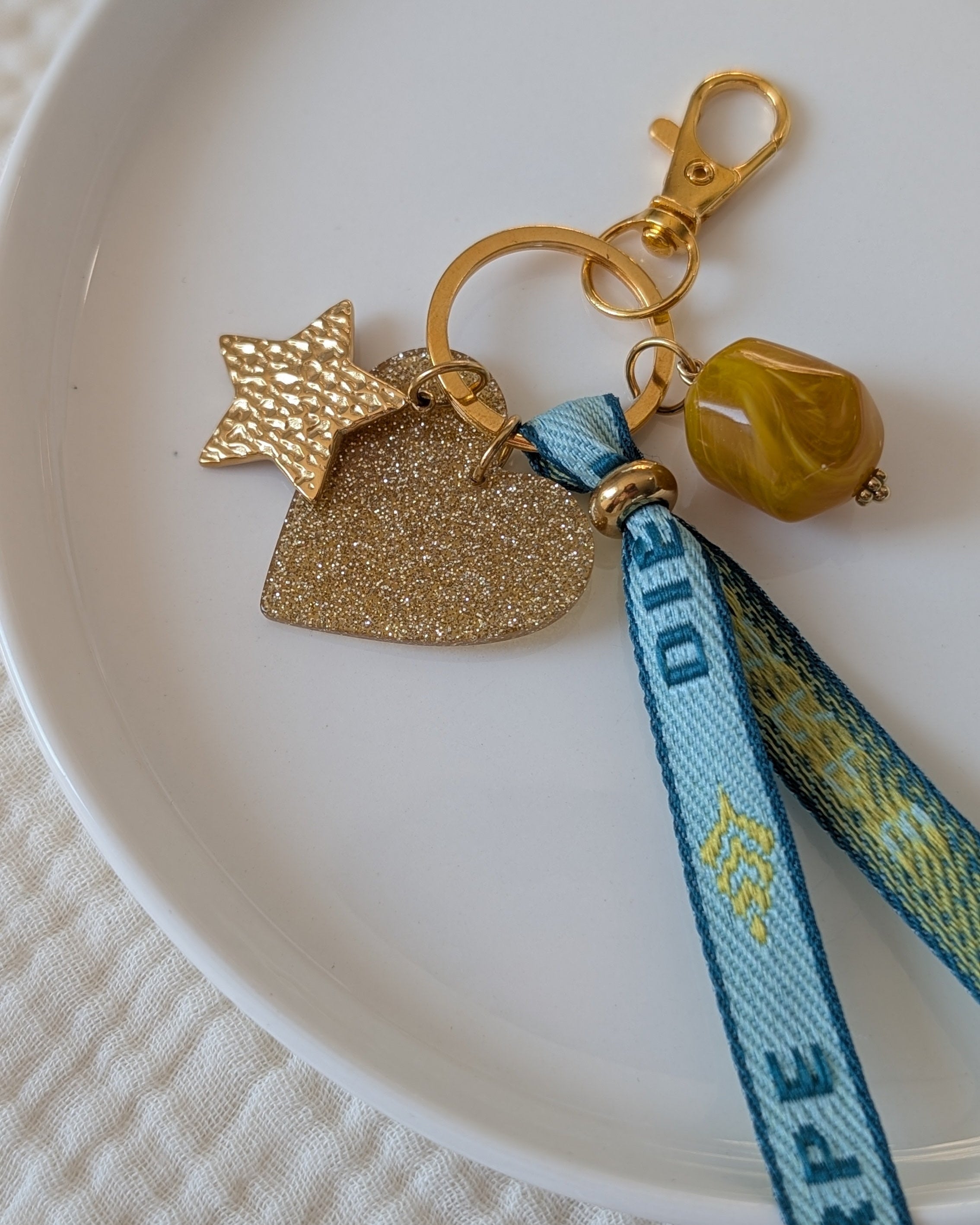 gros plan Porte Clés ou bijoux de sac avec ruban bleu mot carpe diem. Pendentif coeur à paillettes doré étoile acier inoxydable et perle résine marbré jaune. Créations La Tête dans les Nétoiles