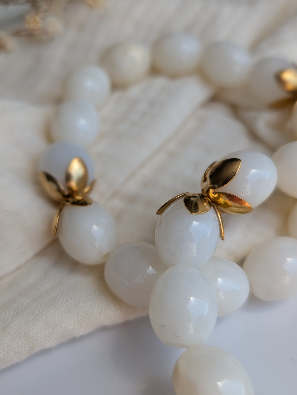 Gros plan sur les coupelles de fleurs dorées en acier inoxydable du bracelet Olivia en blanc nacré. Créations artisanales La Tête dans les nétoiles