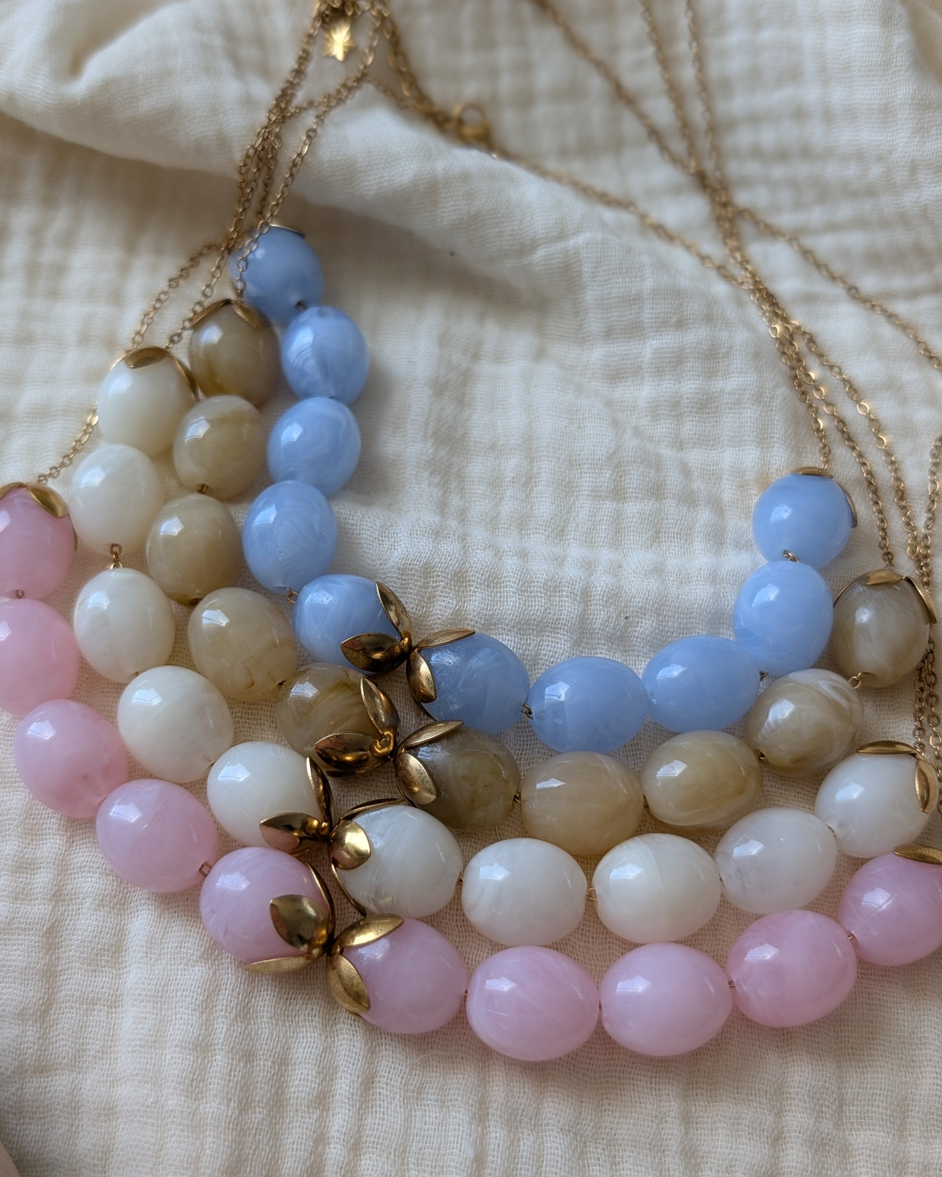 Les 4 coloris du collier perles résine Olivia, bleu azur, rose poudré, blanc et beige marbré. Créations Artisanales La Tête dans les Nétoiles