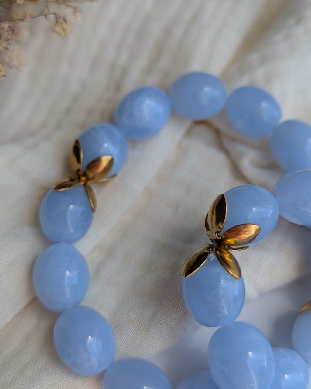 Gros plan sur les détails doré du bracelet Olivia perles résine bleu marbré et acier inoxydable. Posés sur gaze de coton. Créations artisanales La Tête dans les Nétoiles