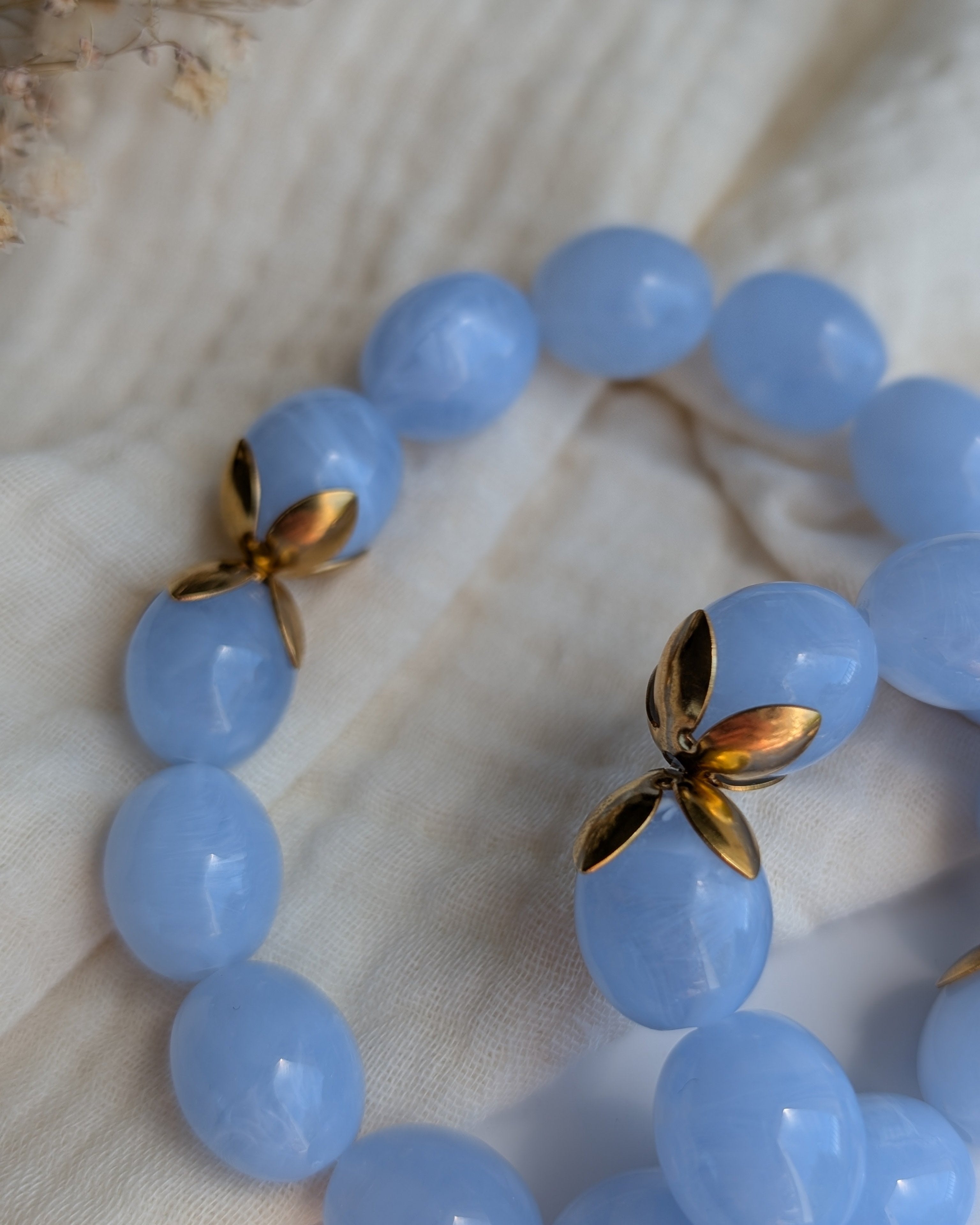 Gros plan sur les détails doré du bracelet Olivia perles résine bleu marbré et acier inoxydable. Posés sur gaze de coton. Créations artisanales La Tête dans les Nétoiles